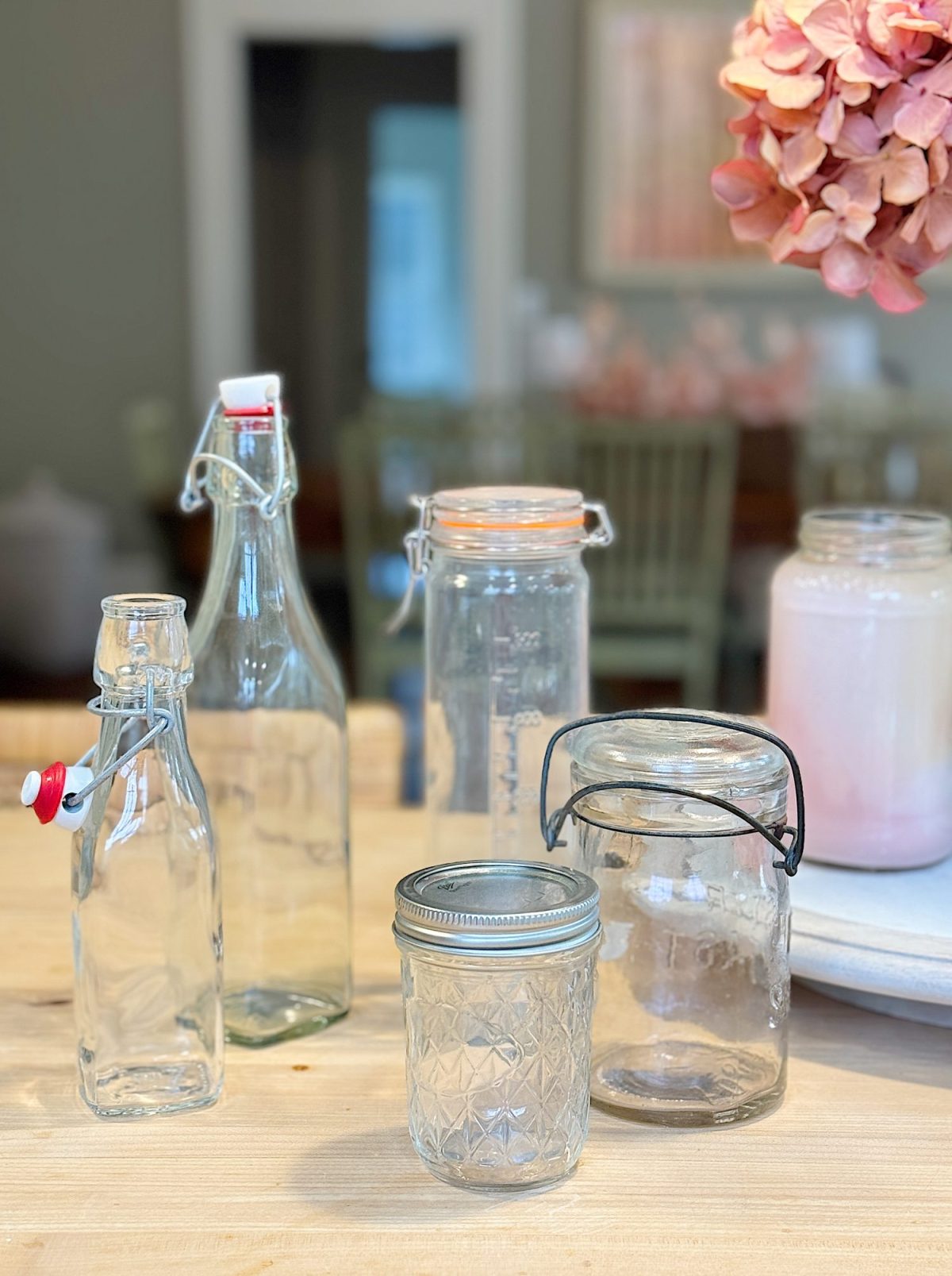 Various empty glass jars and bottles with metal clasps and lids are displayed on a wooden table indoors.