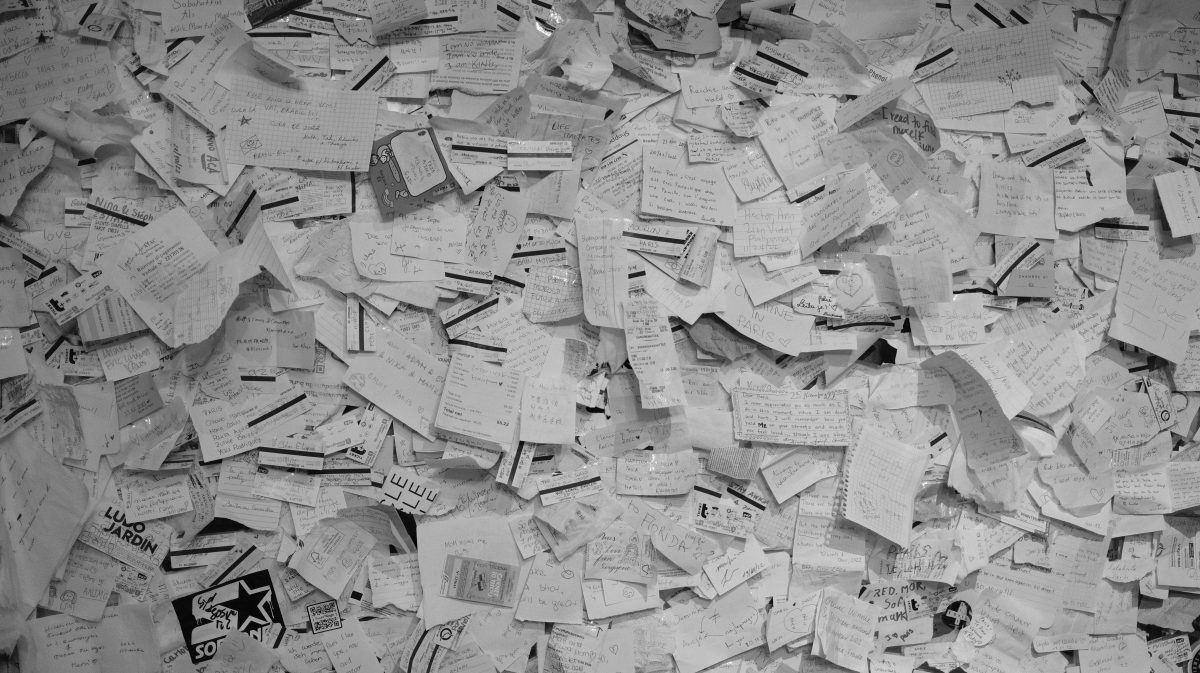 A wall covered with numerous overlapping handwritten notes and papers in black and white.