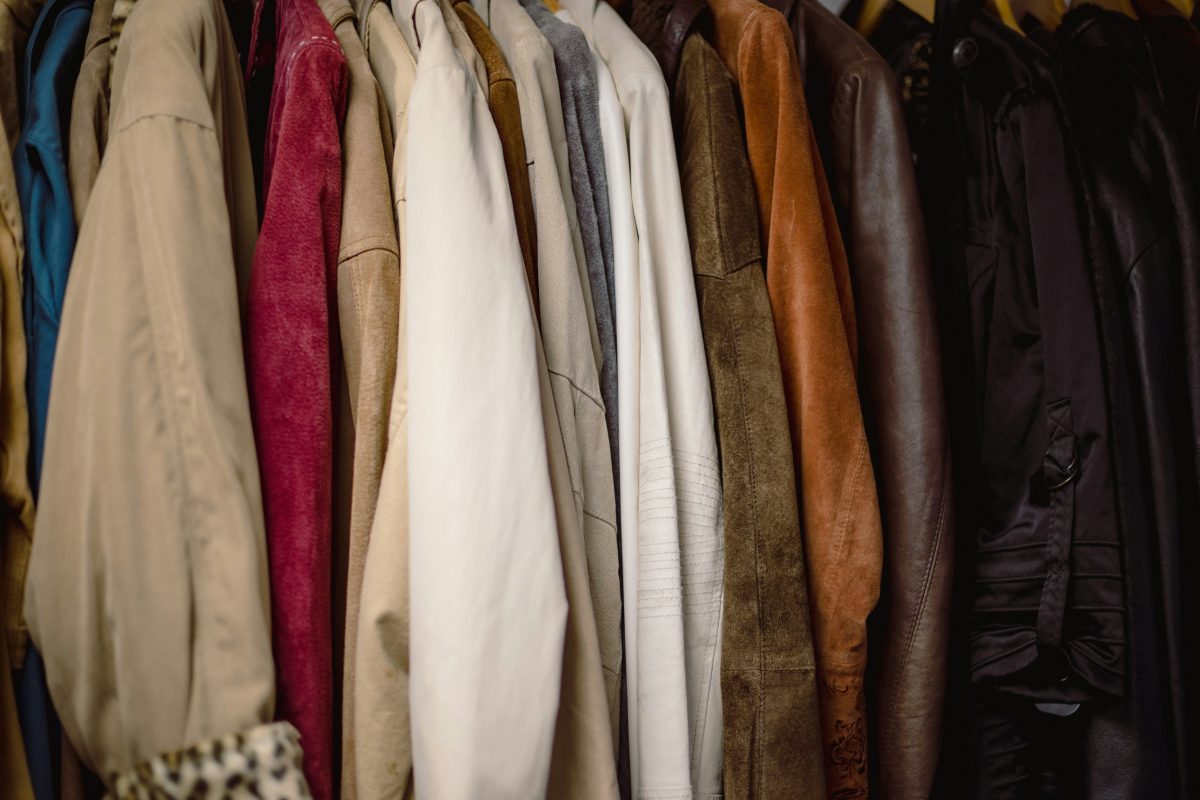 A row of various colored coats hanging on a rack, featuring different materials and textures.