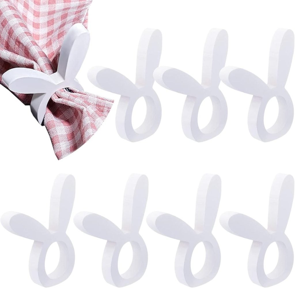 Seven white plastic napkin rings shaped like bunny ears, perfect for Easter decor, with one holding a pink and white checkered napkin.
