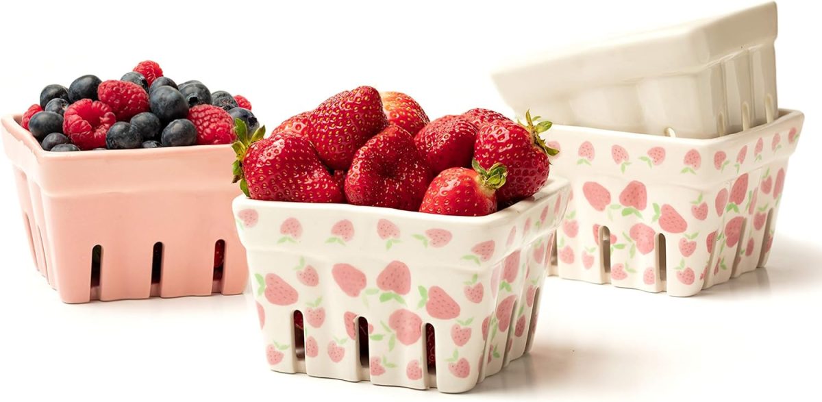 Ceramic berry baskets with strawberry patterns hold strawberries, blueberries, and raspberries. An empty basket is in the background.
