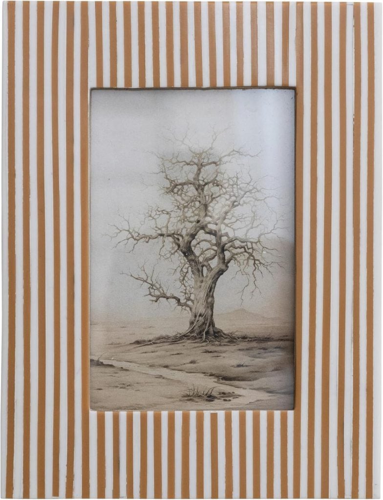 A framed black and white drawing of a leafless tree, set in a frame with vertical brown and white stripes&mdash;an elegant choice for spring decor.