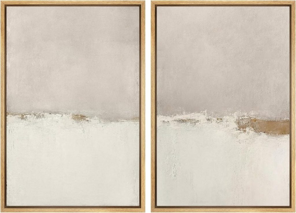 Two pieces of abstract wall art in light neutral tones, each showcasing a textured beige upper half, a white lower half, and framed in light wood.