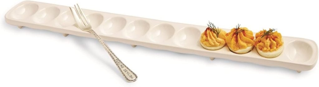 A long white ceramic deviled egg tray holds three deviled eggs with garnish beside a small metal serving fork, perfect for showcasing your Best Deviled Eggs Recipe.