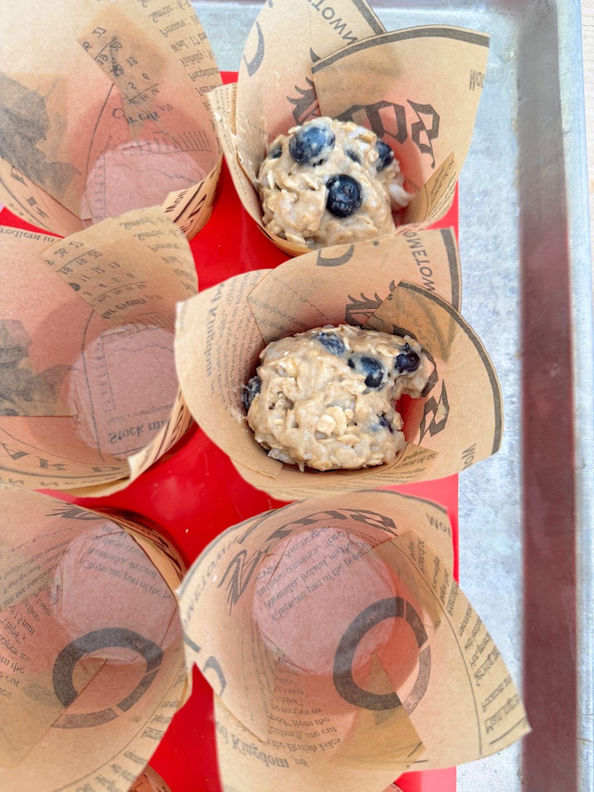 Muffin liners in a tray, two containing unbaked blueberry muffin batter.