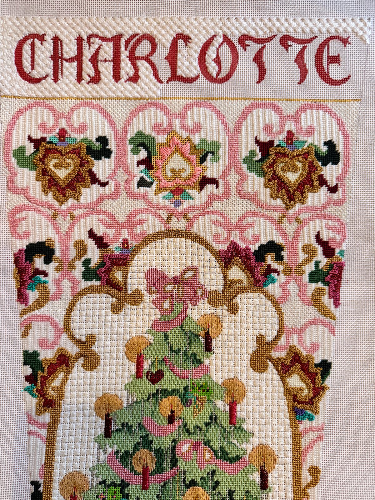Cross-stitched tapestry featuring the name "Charlotte" at the top, ornamental patterns, and a decorated Christmas tree with a bow.