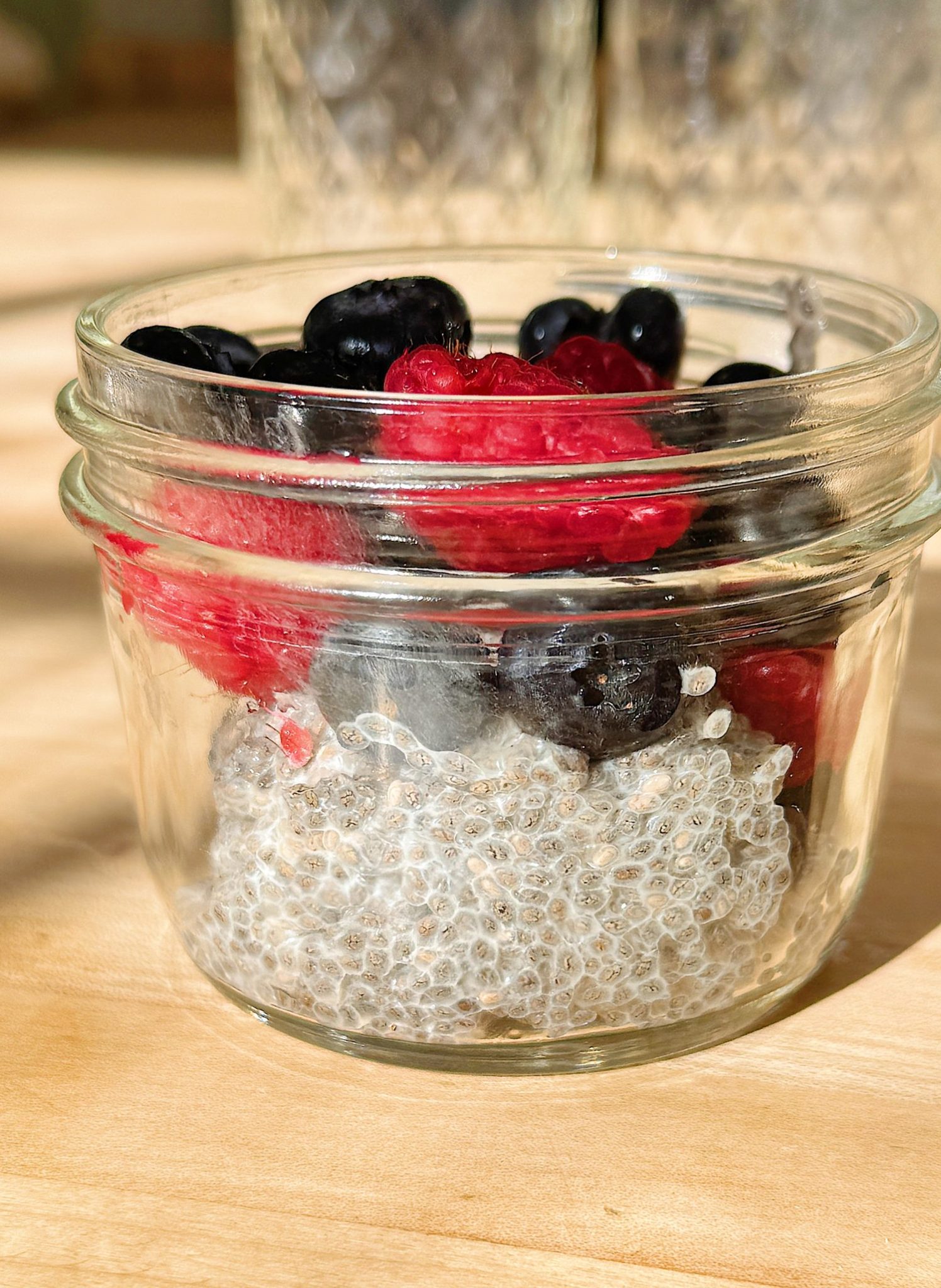 A glass jar filled with chia pudding, topped with blackberries and raspberries, set on a wooden surface.