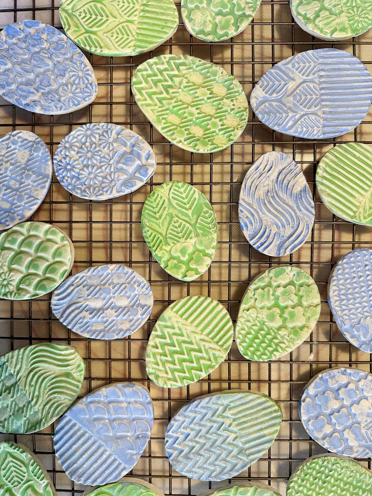 Oval-shaped cookies with green and blue patterned icing are arranged on a wire cooling rack.