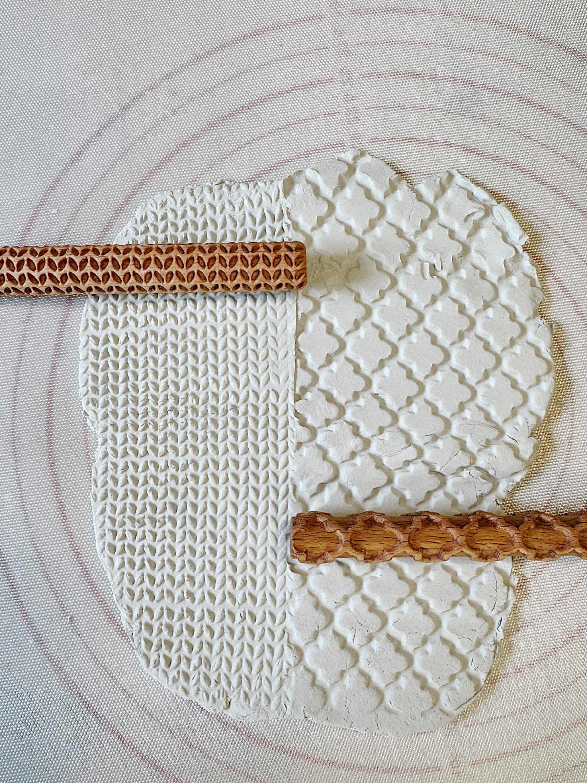 Textured clay slab with two rolling pins on a mat. The left side has a woven pattern, and the right side has a diamond design.