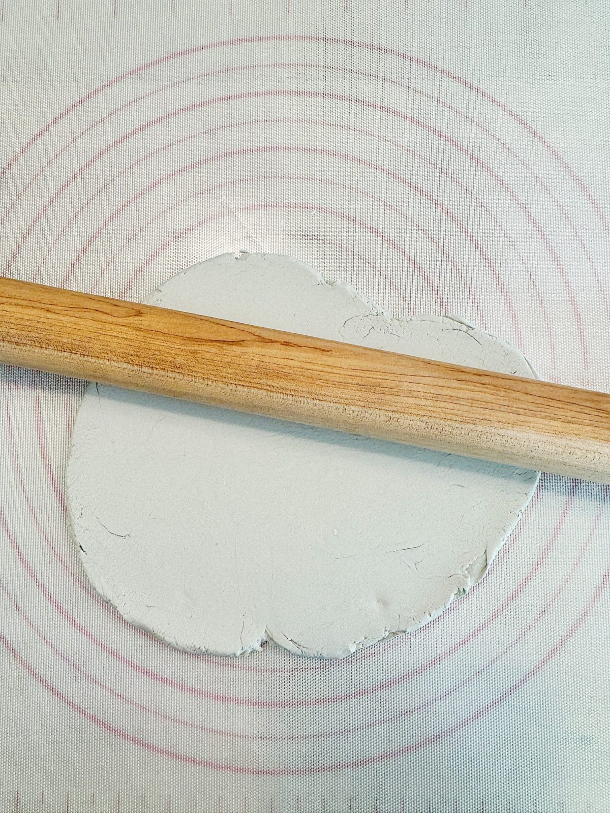 A wooden rolling pin on rolled-out dough, set on a circular marked silicone baking mat.