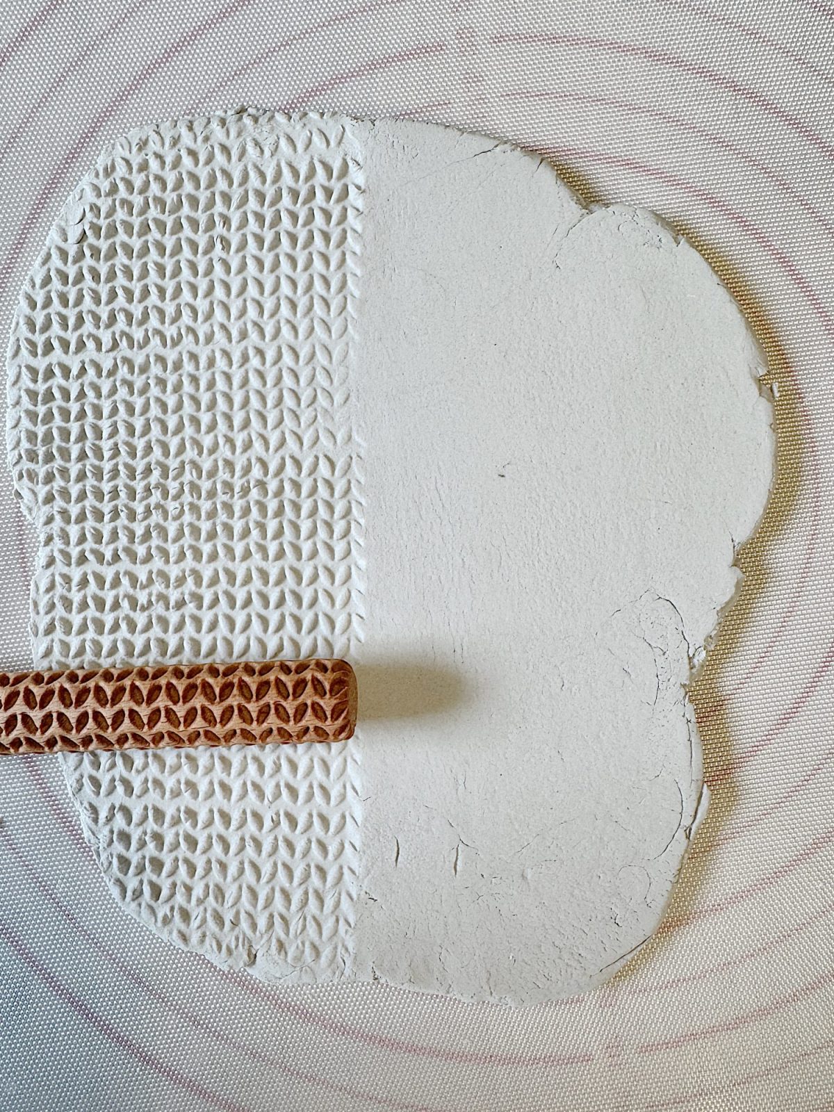 A wooden texture roller creates a herringbone pattern on a slab of white clay.