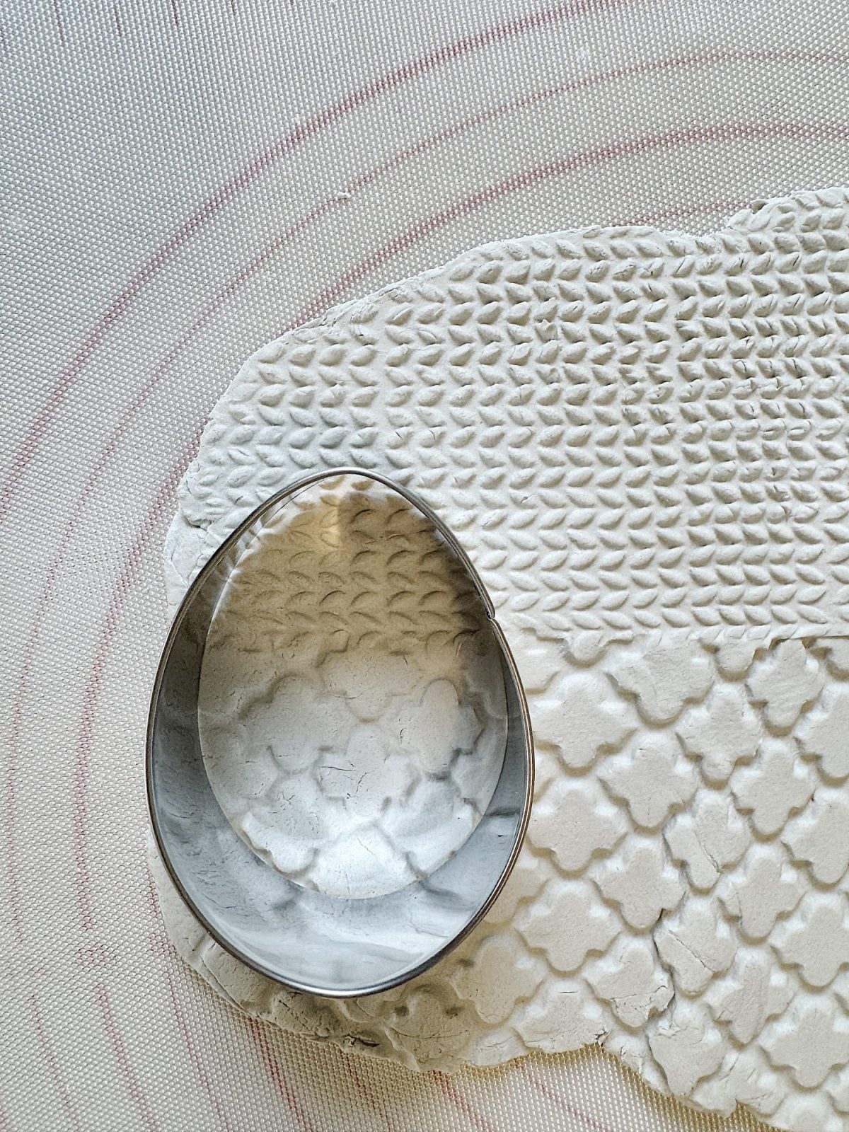 A metal cookie cutter rests on partially rolled out dough with a textured pattern on a silicone baking mat.