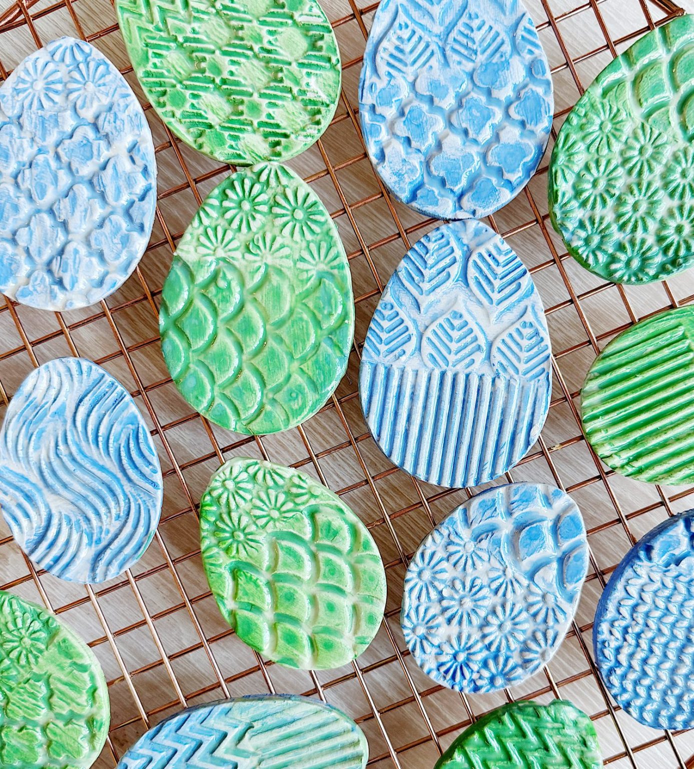 Blue and green textured ceramic egg shapes on a wire cooling rack.