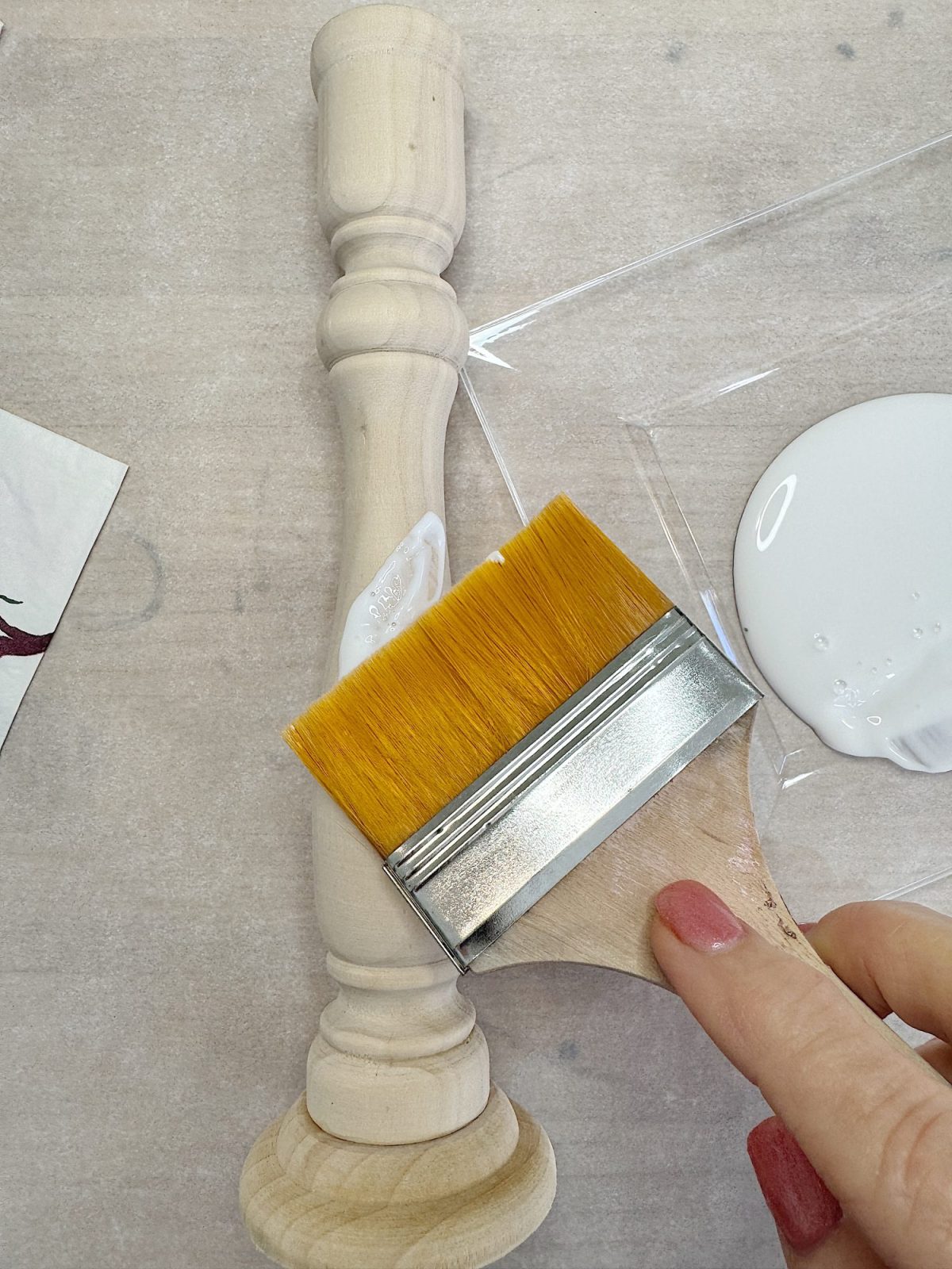 Person applying glue to a wooden candlestick holder with a flat brush on a light surface.