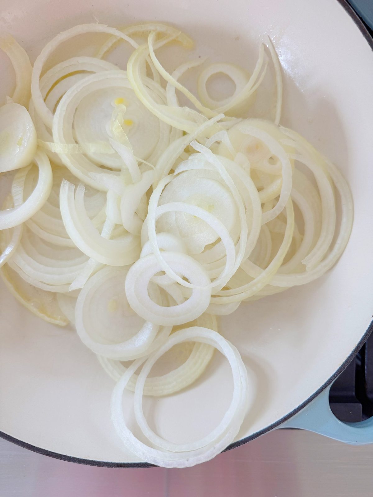 Thinly sliced onions in a light-colored pan.