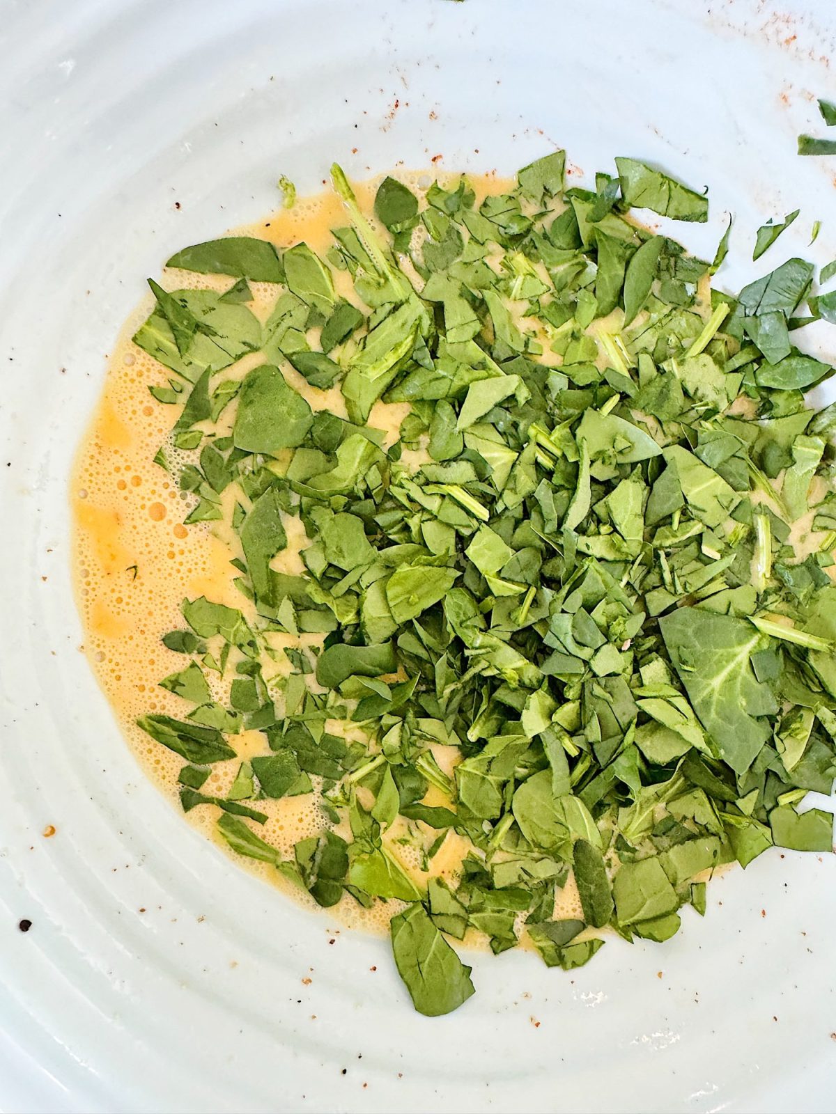 Chopped spinach mixed with beaten eggs on a white plate, ready for cooking.