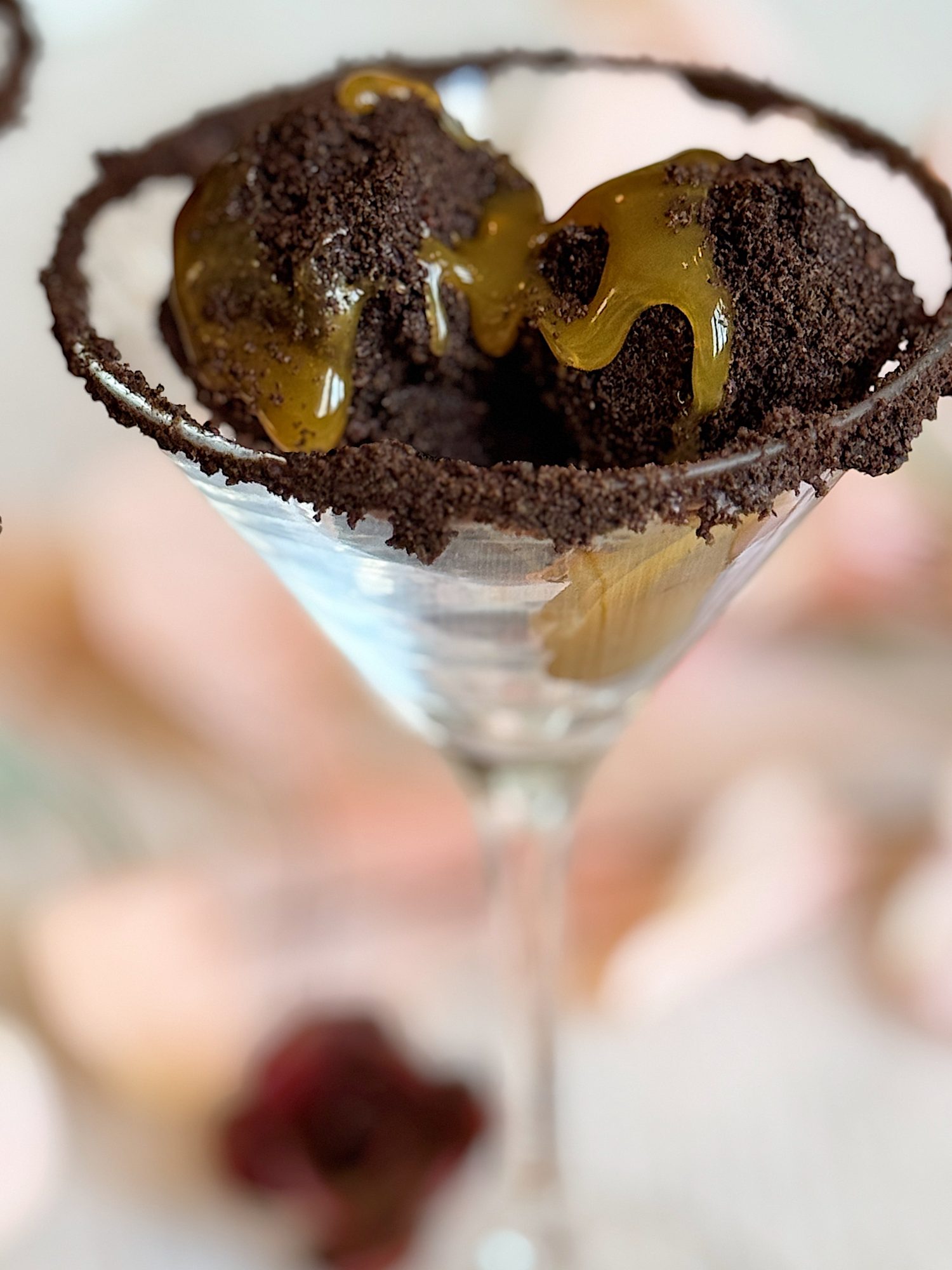 Chocolate truffles with a glossy syrup are served in a glass rimmed with cookie crumbs, creating an elegant dessert presentation.