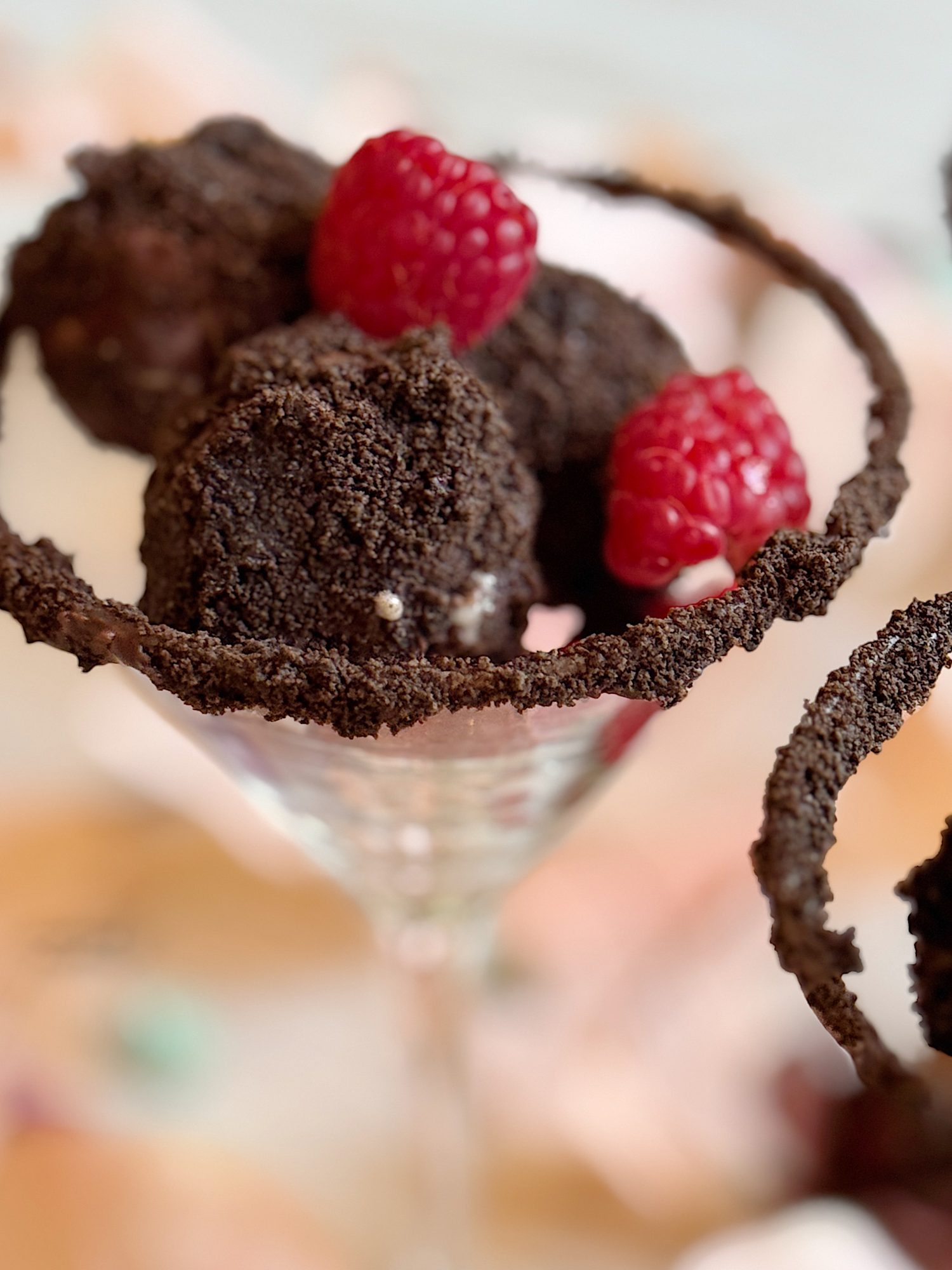 Three chocolate truffles garnished with raspberries in a glass with a chocolate crumb rim.