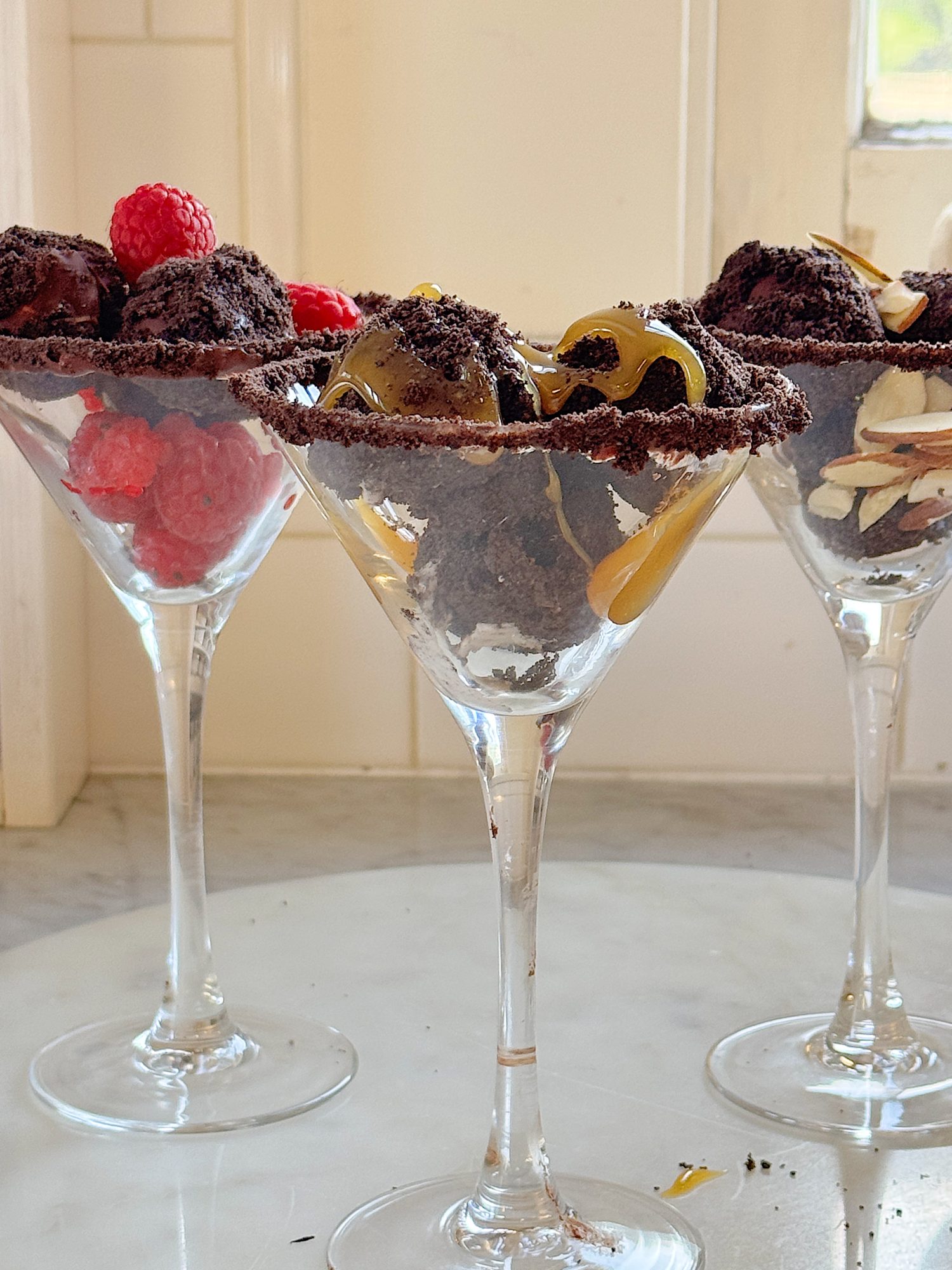 Three martini glasses with a dessert comprising chocolate, raspberries, caramel, and almonds on a tabletop.