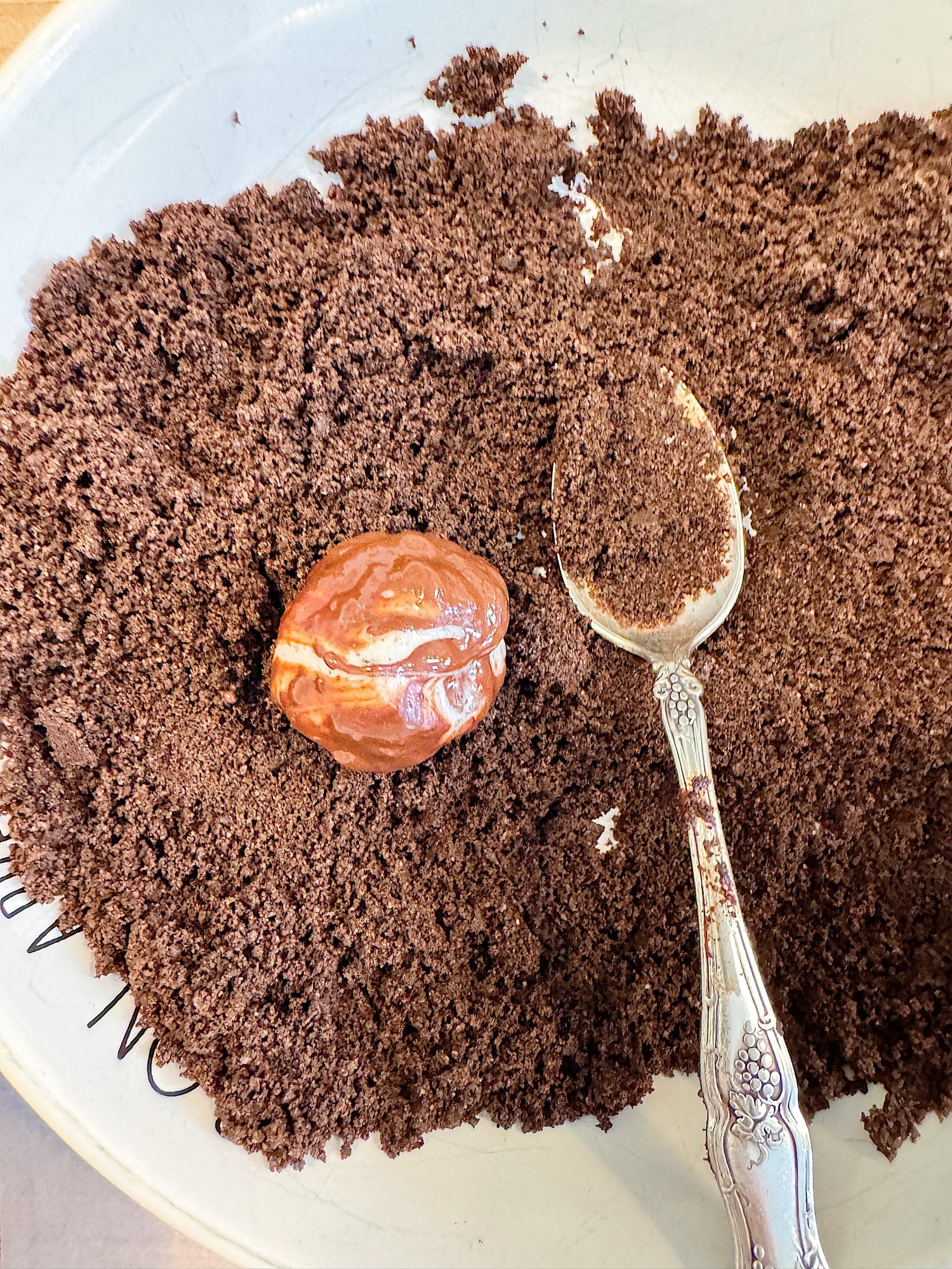 A bowl of finely ground coffee with a silver spoon resting inside. A whole nutmeg sits on top of the coffee grounds.