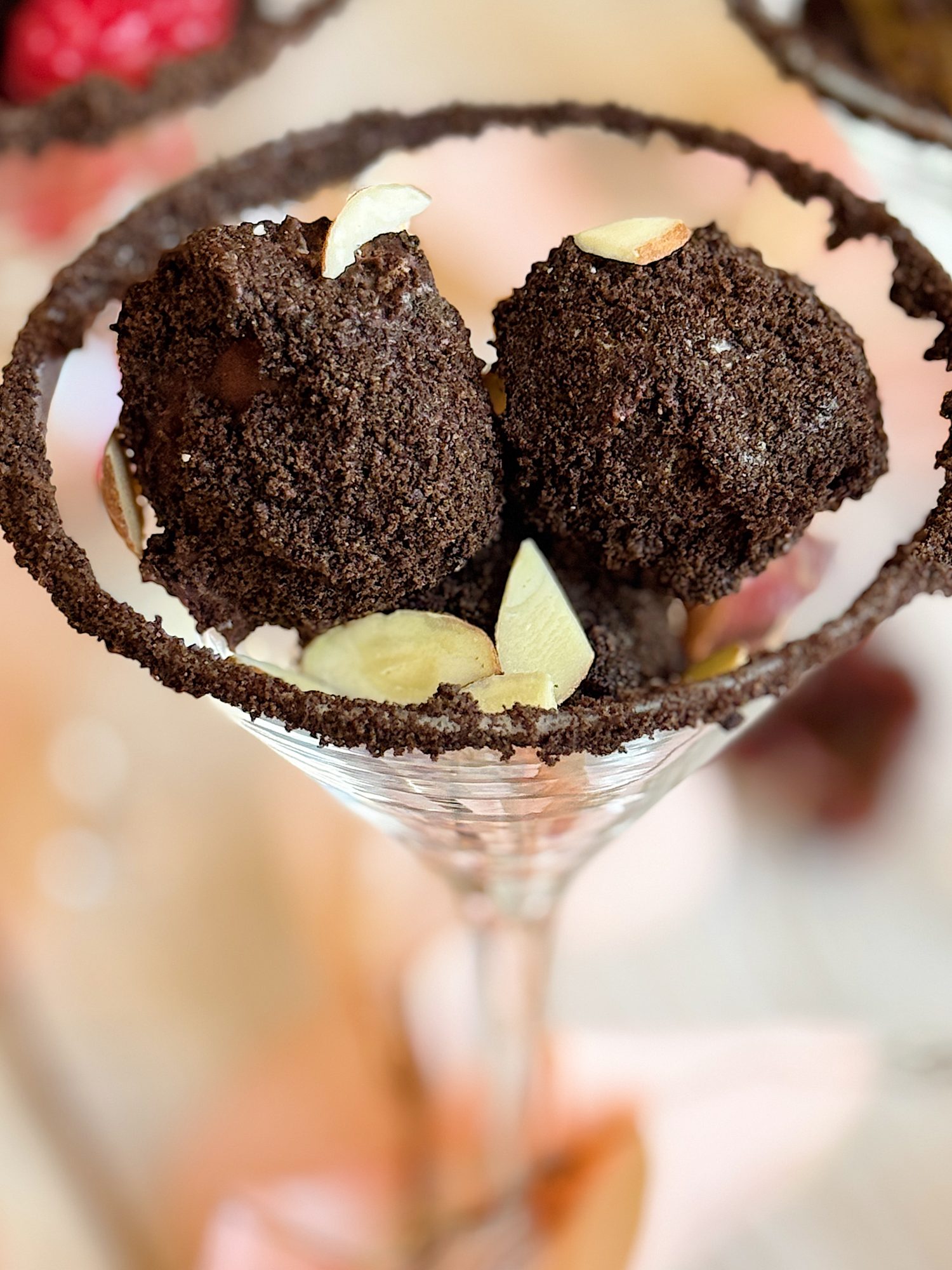 Chocolate truffles with almond slices in a martini glass, rimmed with chocolate crumbs on a blurred background.