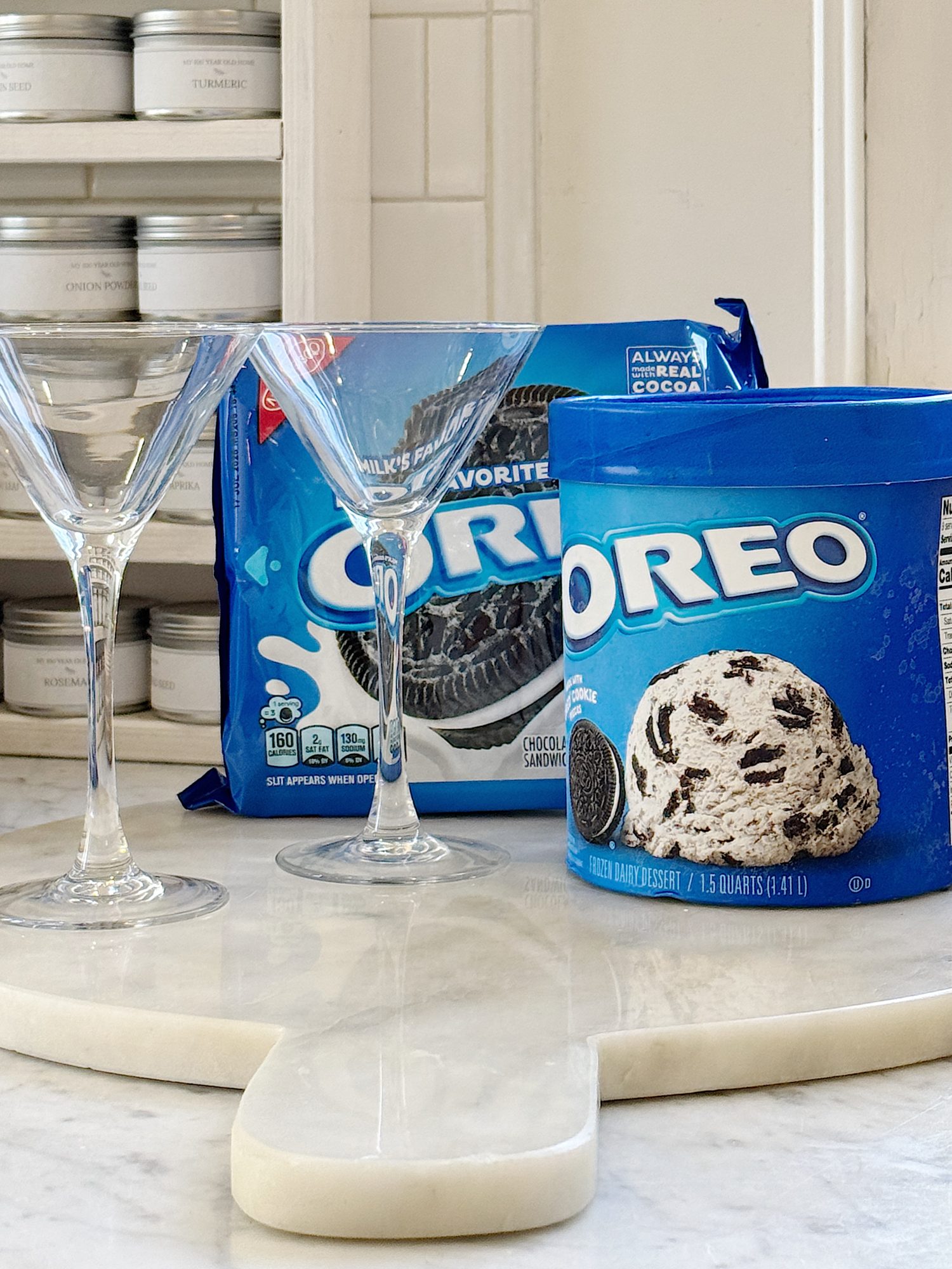 Two empty martini glasses next to a pack of Oreo cookies and a tub of Oreo ice cream on a white countertop.