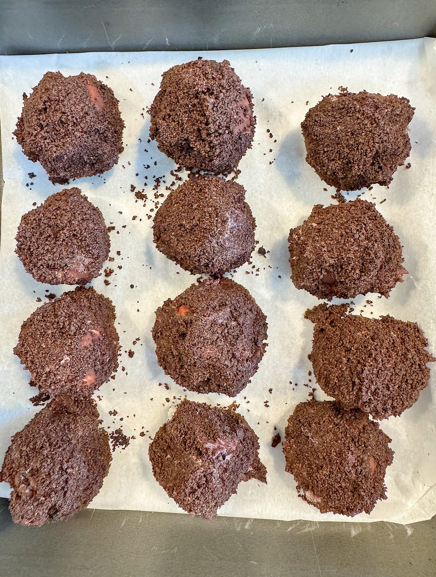 Twelve chocolate-coated balls on a parchment-lined baking tray.