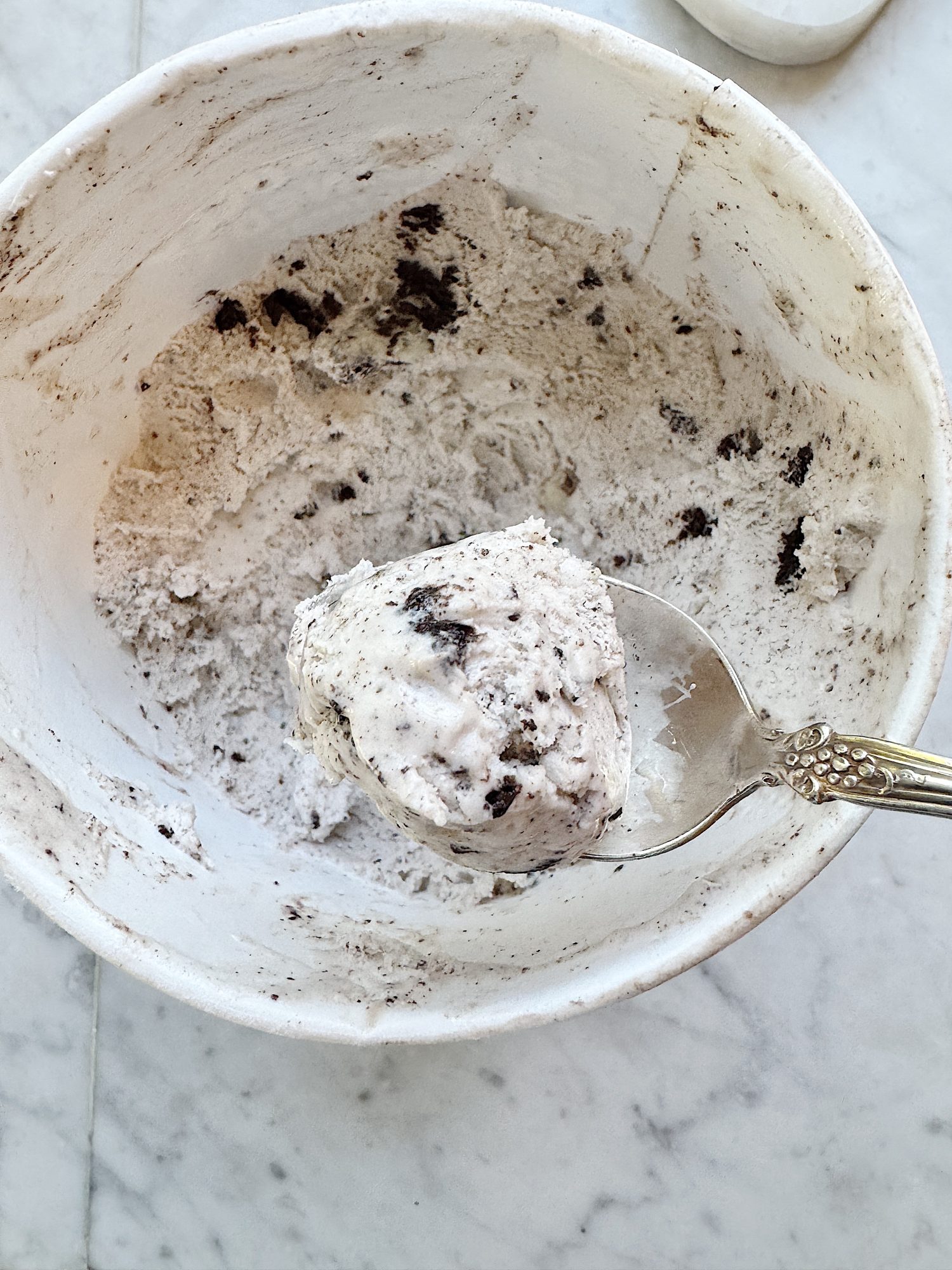 A spoon scoops cookies and cream ice cream from a partially empty container on a marble surface.