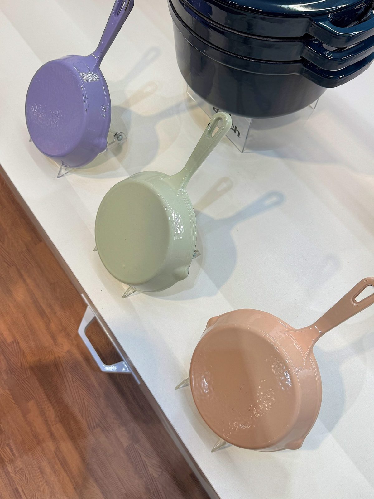 Three ceramic pans in purple, green, and beige are displayed on a white surface, viewed from above.
