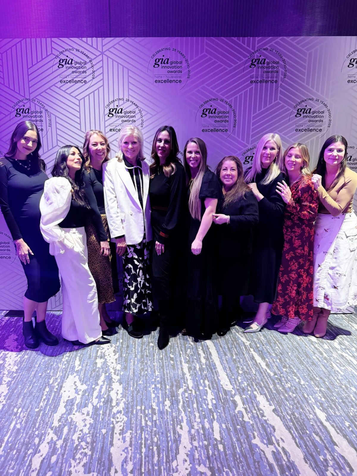A group of ten women posing together in front of a "gia global excellence" backdrop on a patterned carpet.