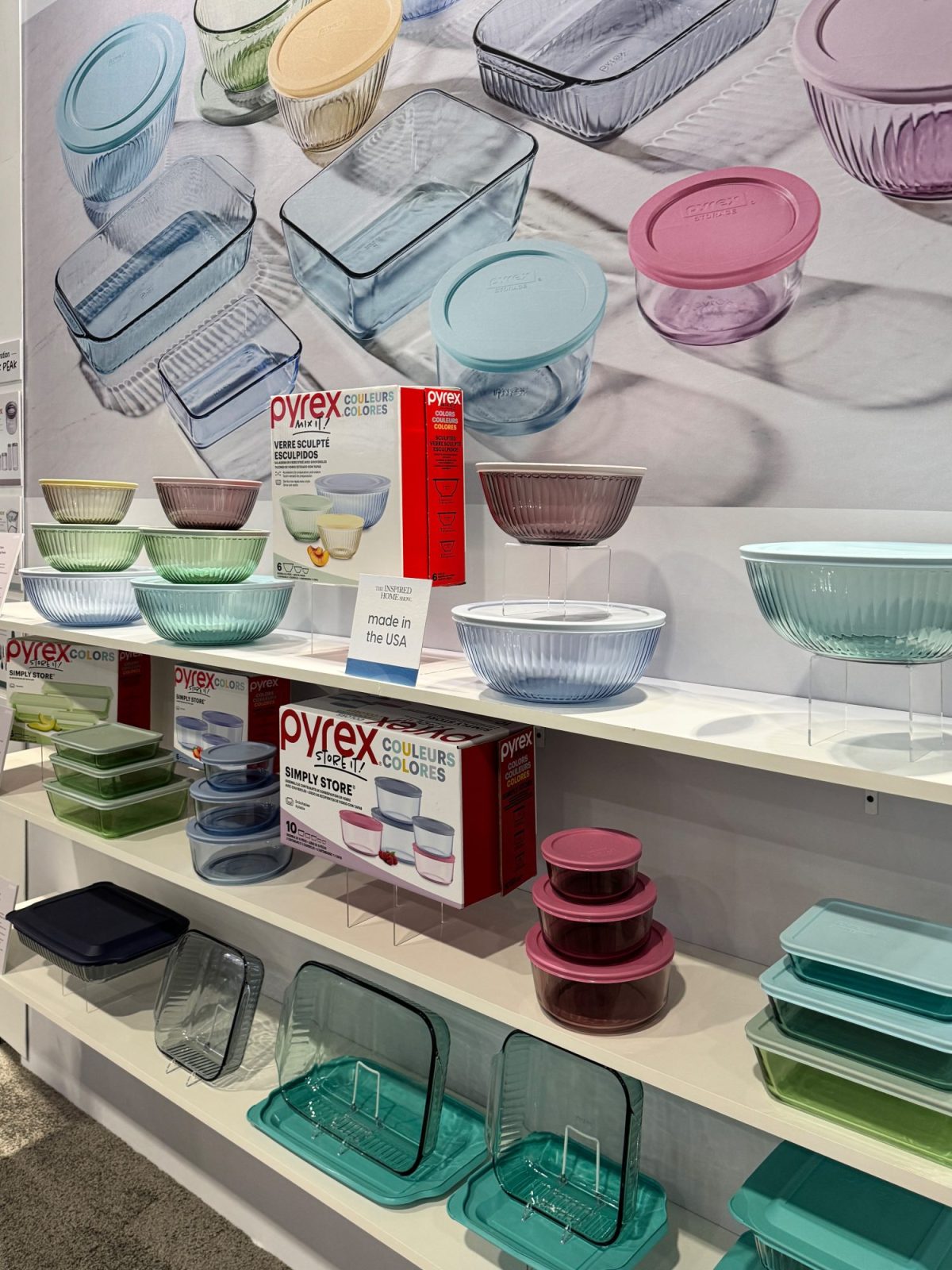 Shelves displaying various glass kitchenware including bowls and baking dishes in pastel colors. Packaging includes Pyrex branding.