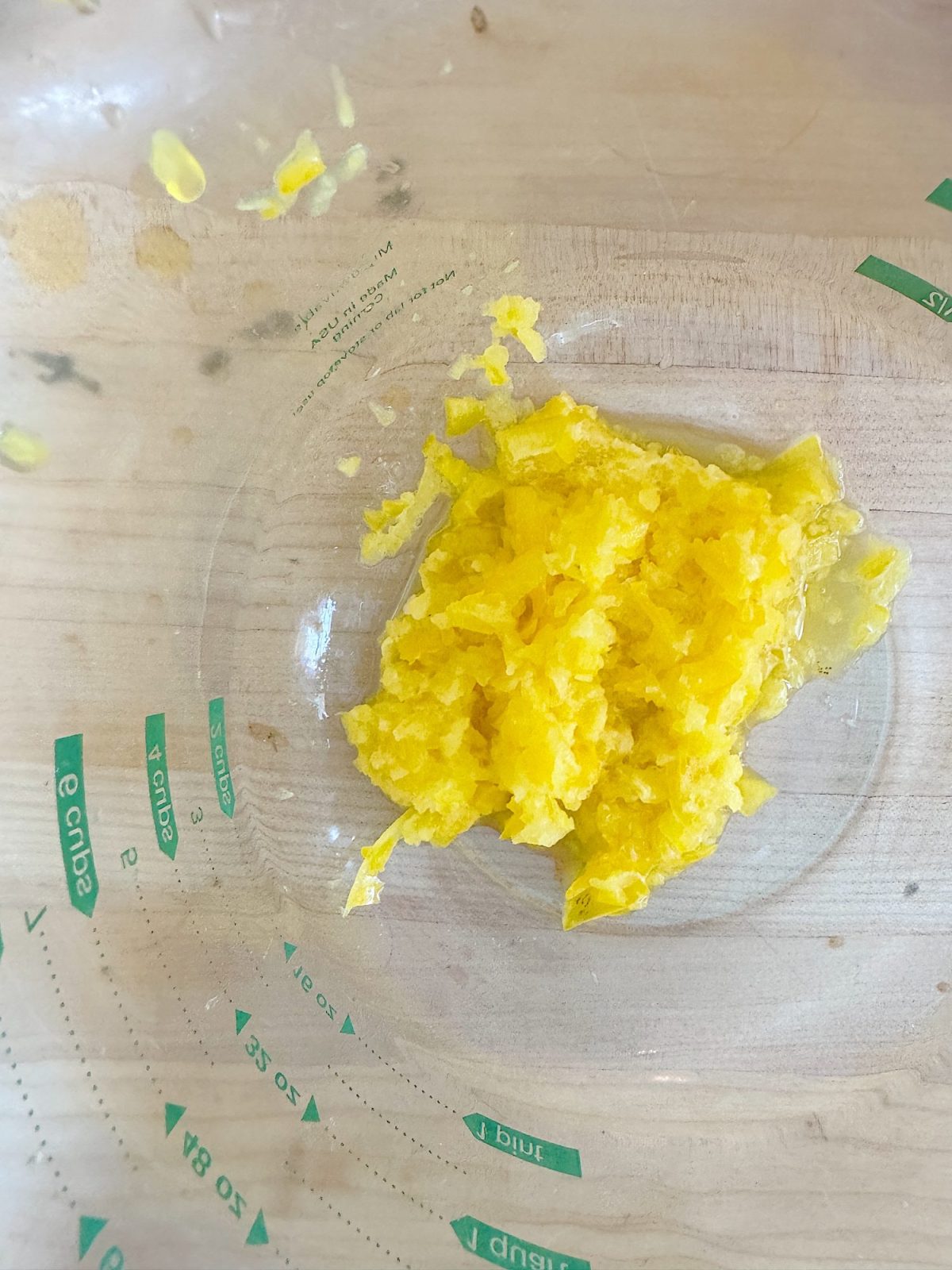 Yellow pulp on the bottom of a translucent measuring cup, placed on a light wooden surface.