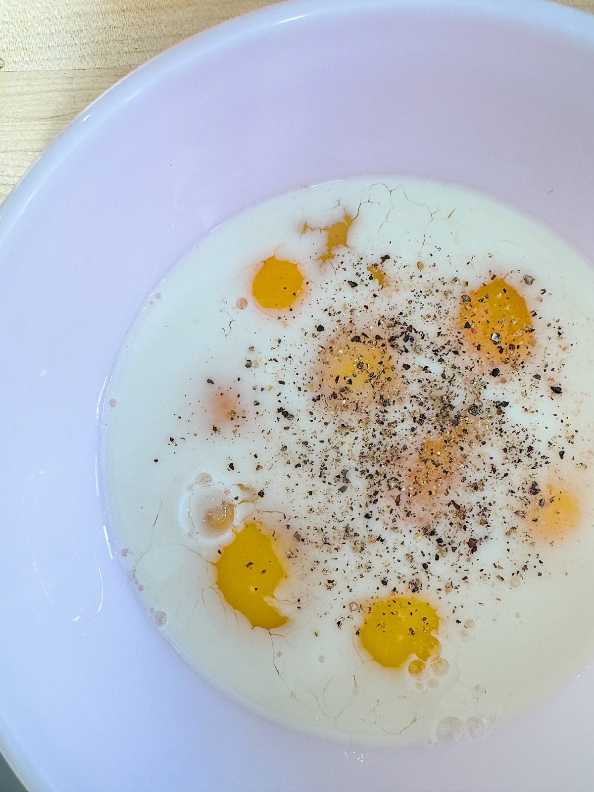 Egg yolks and milk with pepper sprinkled on top in a white bowl.