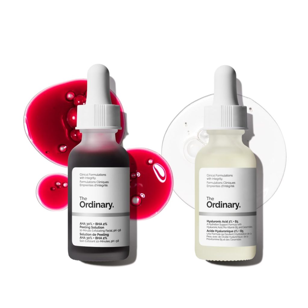 Two dropper bottles from The Ordinary, one with a red AHA 30% + BHA 2% solution and the other a clear Hyaluronic Acid 2% + B5, rest on colored liquid spills&mdash;perfect for refreshing your skin before Easter Brunch.