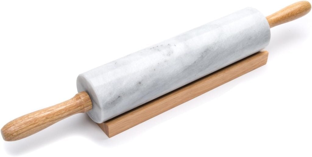 A marble rolling pin with wooden handles, perfect for preparing a blueberry galette, rests on a wooden stand against a white background.
