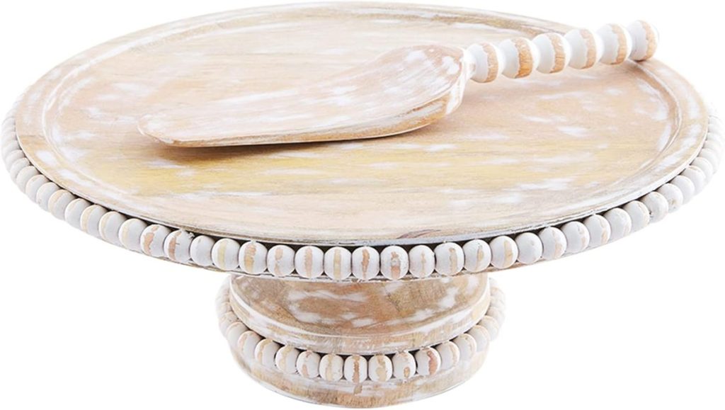 A wooden cake stand with a matching beaded edge and a serving spatula on top, perfect for styling your Airbnb in Waco.