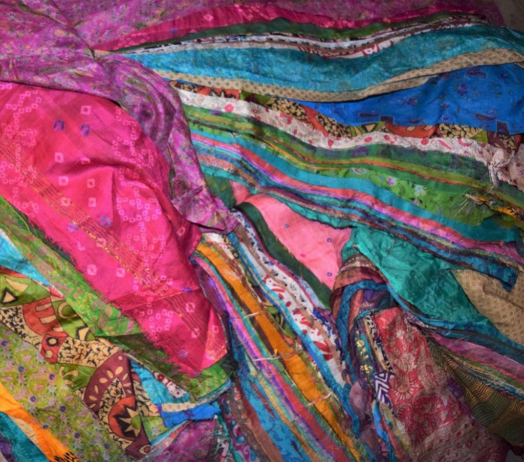 A pile of colorful, patterned fabric pieces in shades of pink, blue, green, orange, and purple, featuring designs and textures reminiscent of decorated Easter eggs.