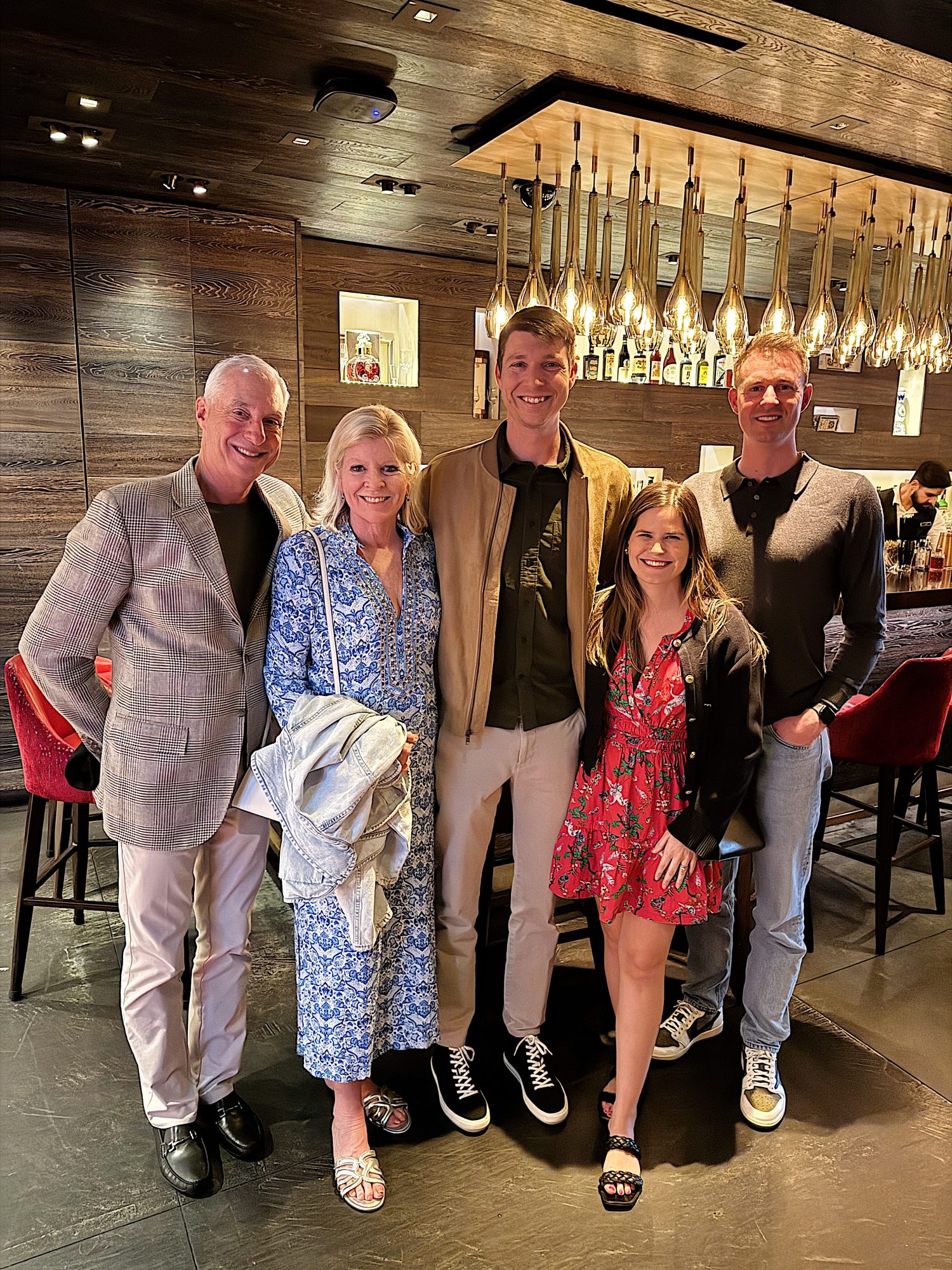 Five people smiling in a restaurant setting with modern decor and pendant lights.