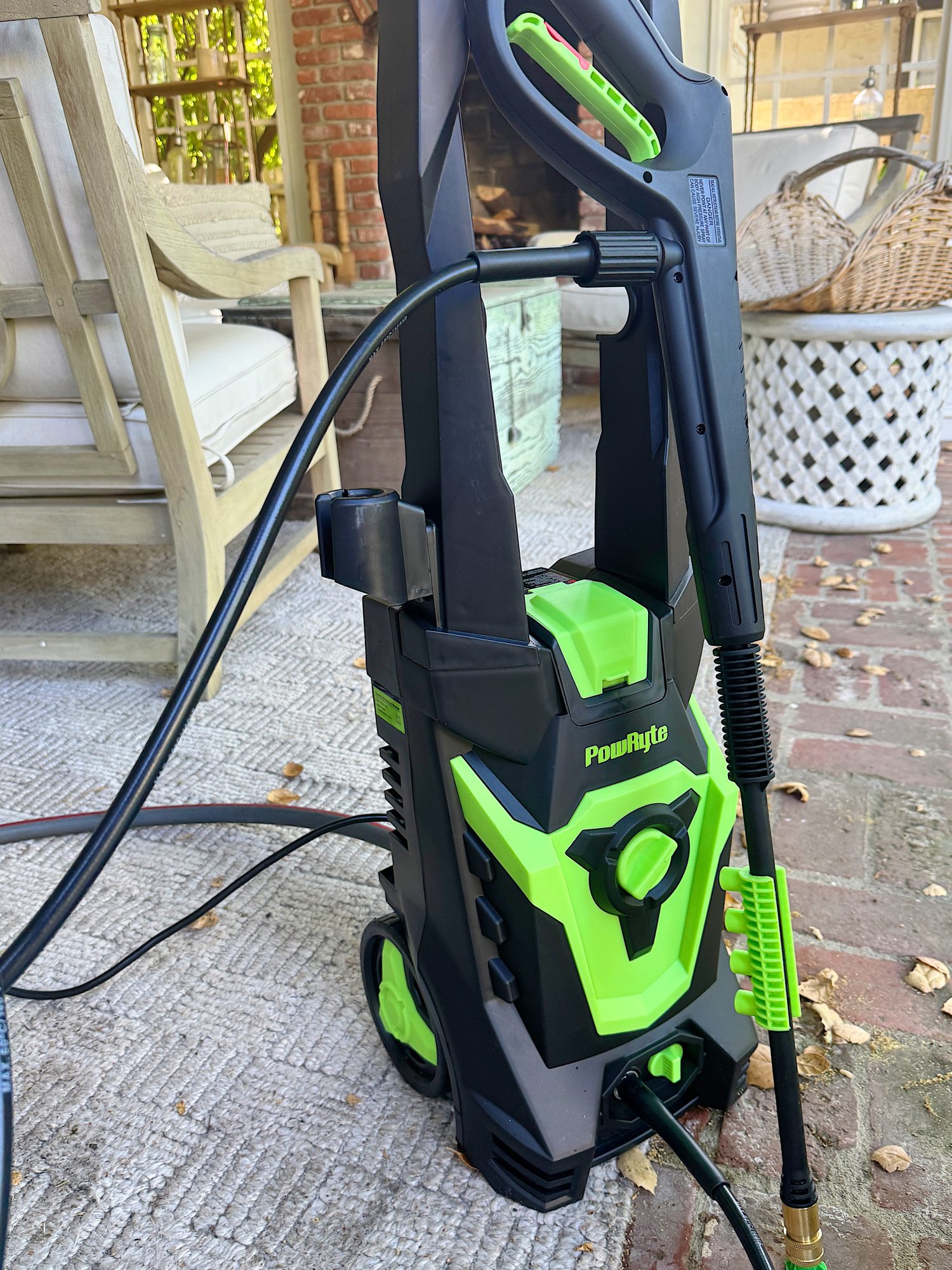A green and black PowRyte pressure washer is placed on an outdoor rug near patio furniture and a brick floor.