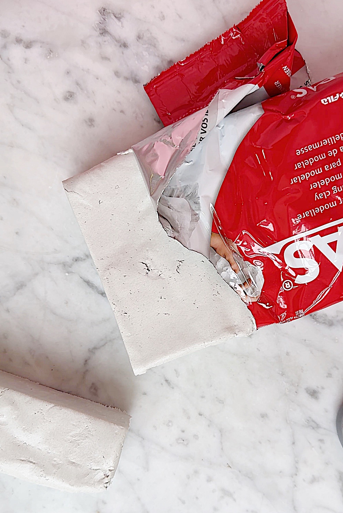 Red and white package of DAS modeling clay partially opened on a marble surface, with a piece of clay cut off and placed next to it.