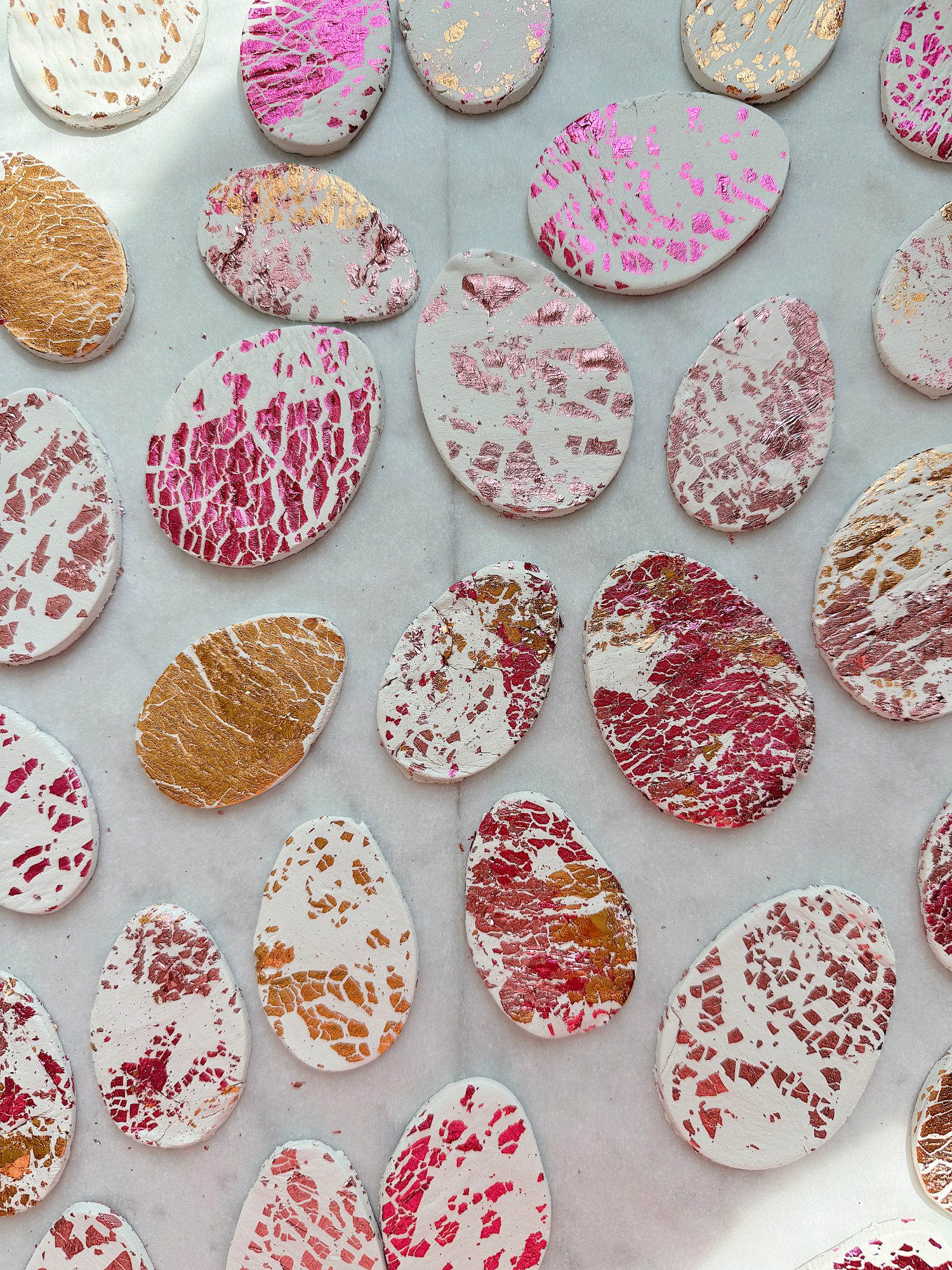 White oval objects with pink, red, and gold abstract patterns scattered on a light surface.