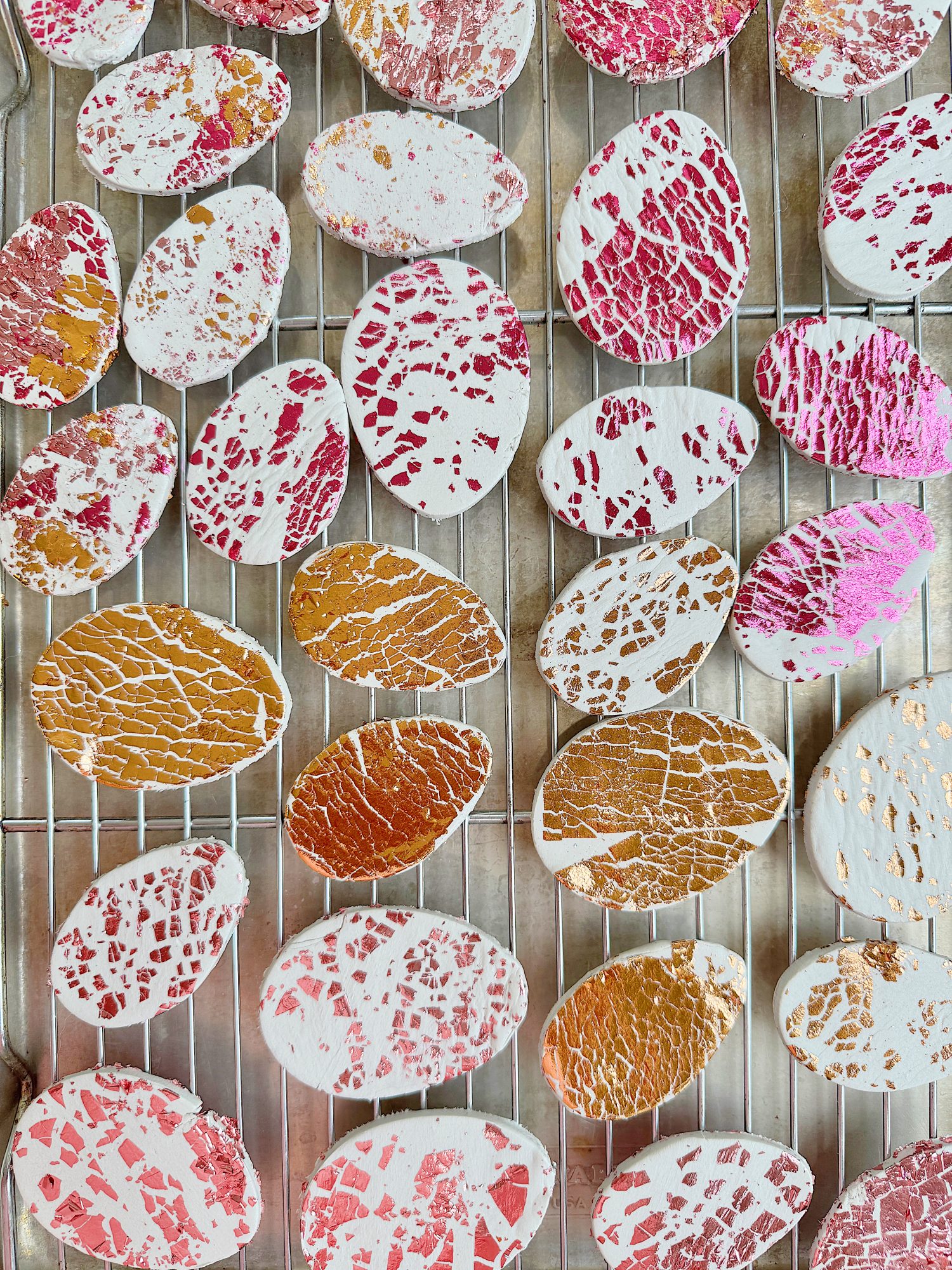 Colorful marbled cookies with pink, gold, and white patterns are placed on a wire cooling rack.