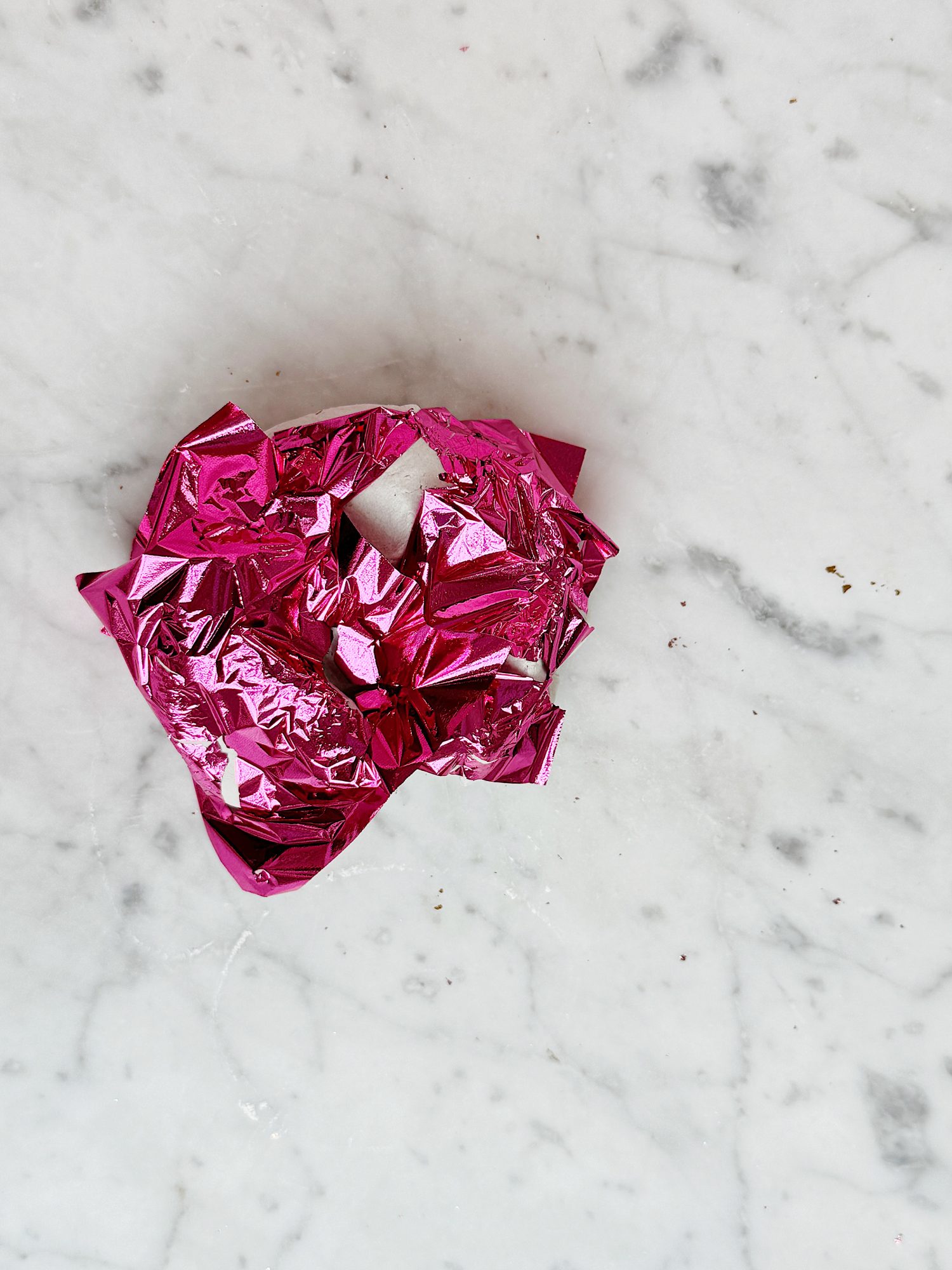 Crumpled pink metallic foil on a white marble surface with visible veins.