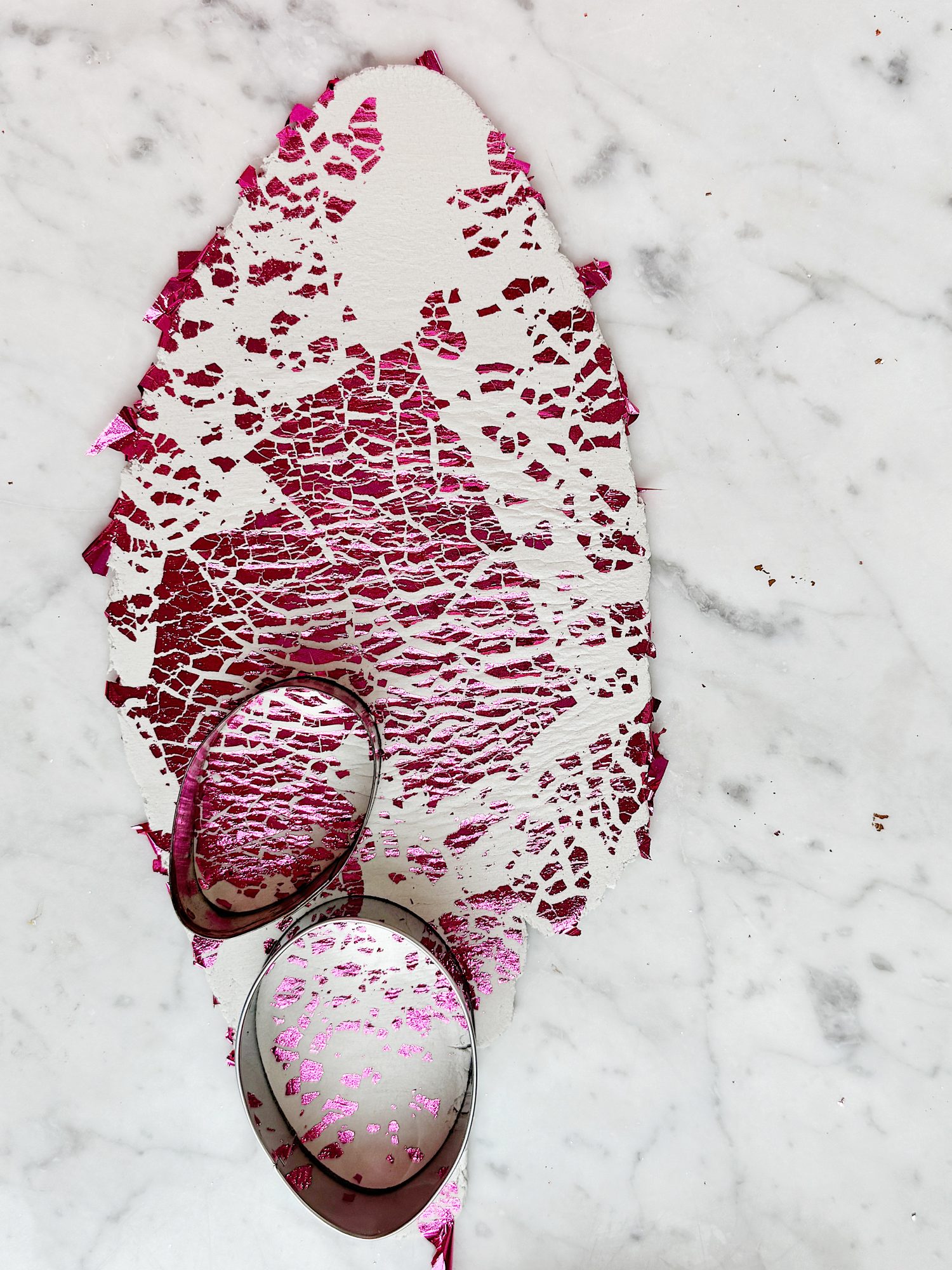 Two metal cookie cutters on a marble surface with a textured sheet of red and pink material, partly cut-out.