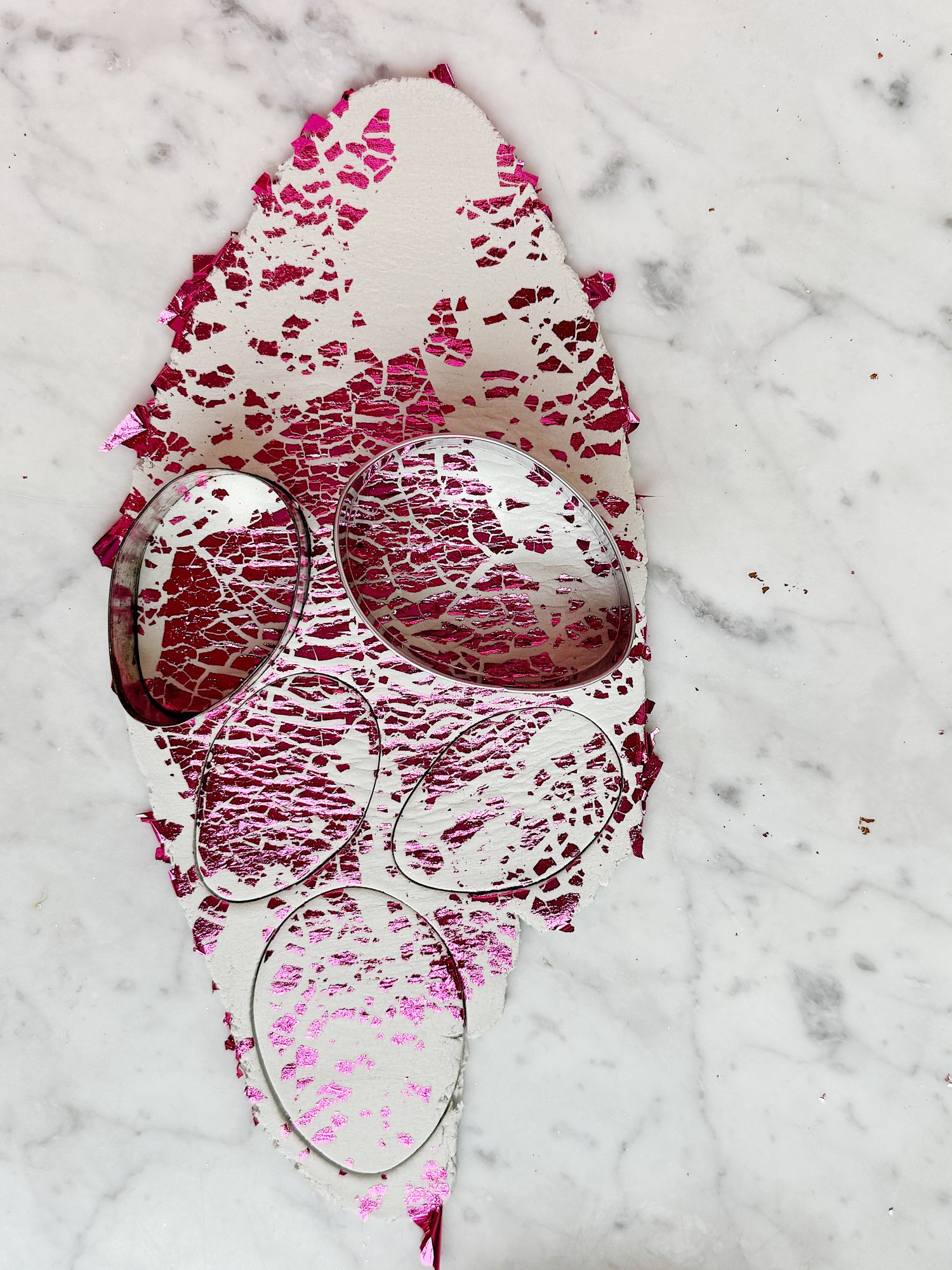 Silver circular cutters on a piece of white material with pink, cracked paint, placed on a marble surface.