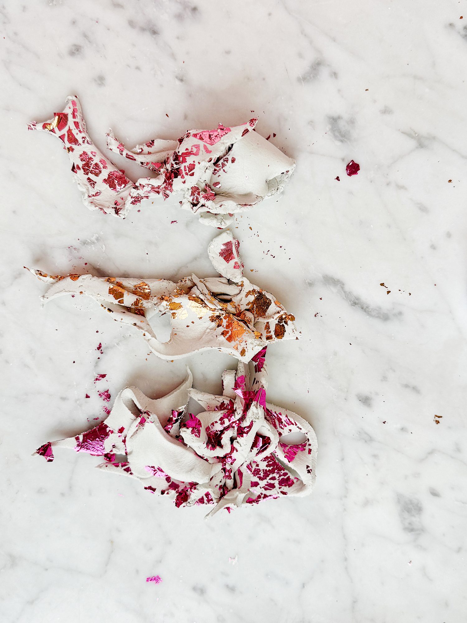 Three paint-splattered, discarded pieces of masking tape rest on a white marble surface.