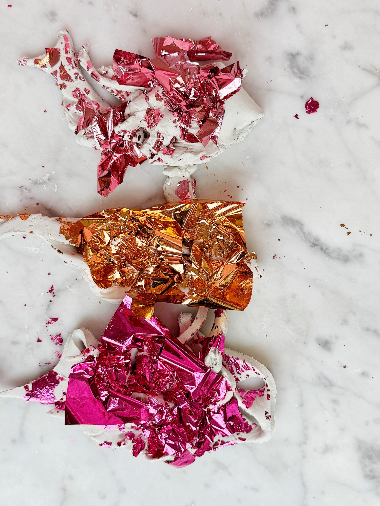 Torn metallic pink, red, and orange foil pieces scattered on a white marble surface.