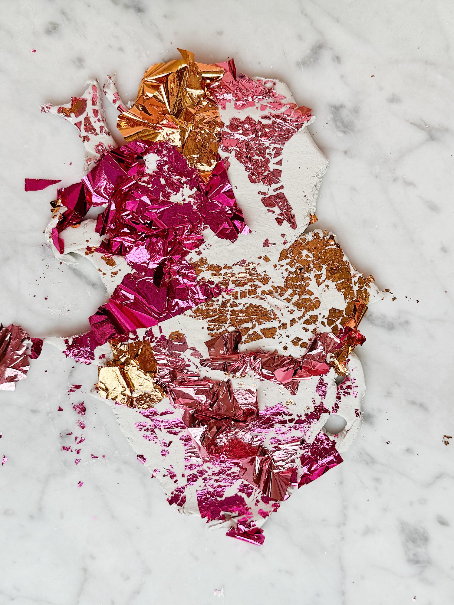 Pink, gold, and copper metallic foil fragments scattered on a white marble surface.