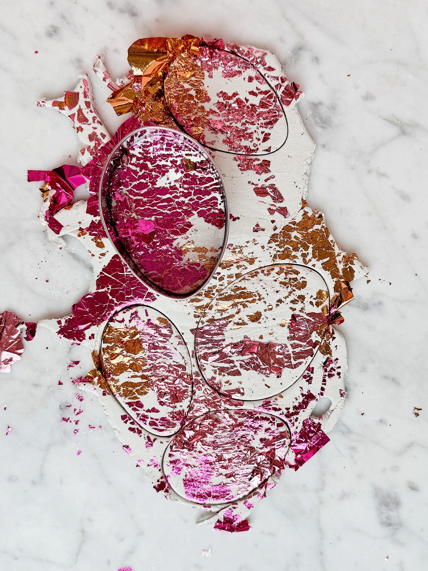 Colorful metallic foil fragments in shades of pink and gold scattered on a white marble surface.