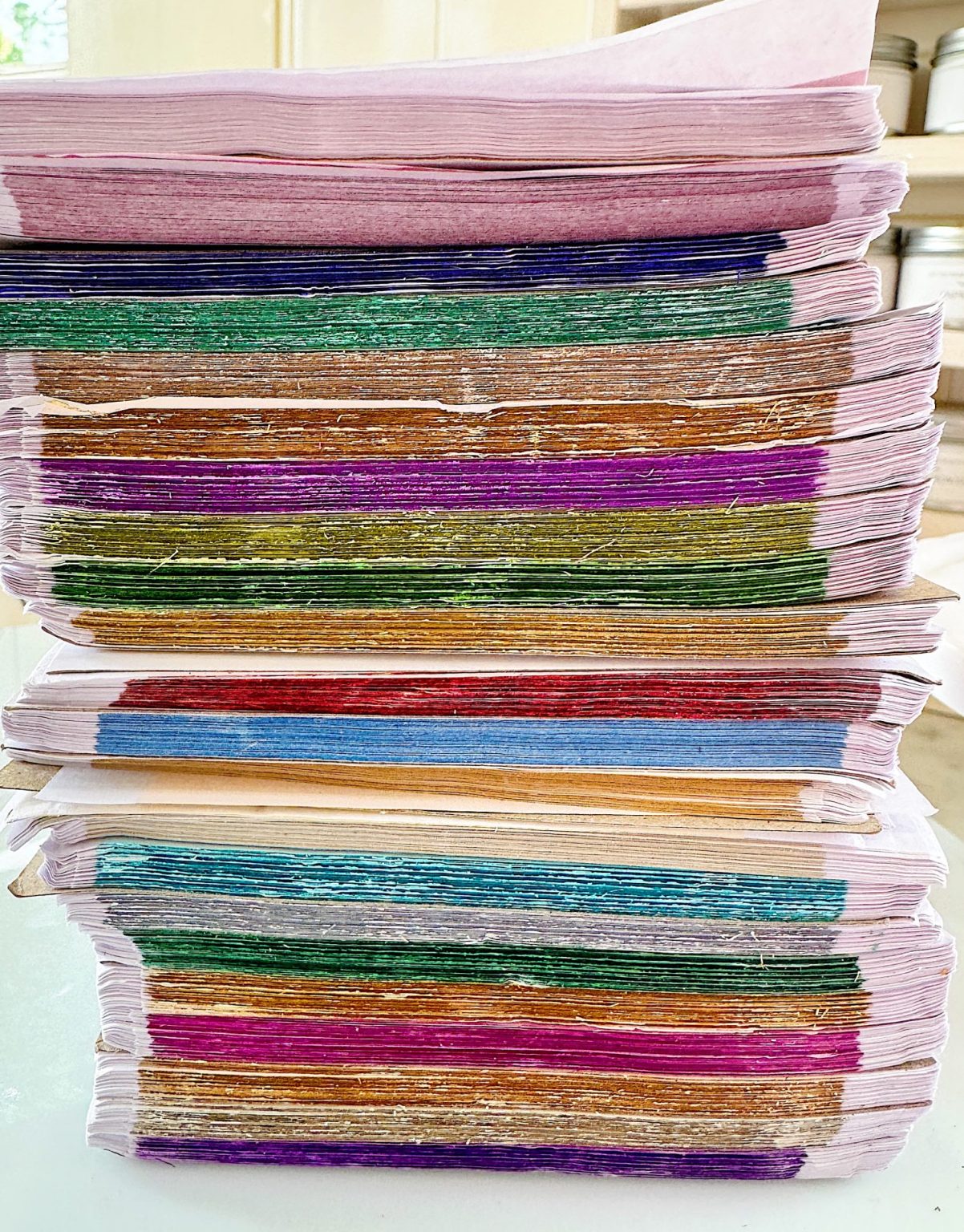 Stacks of colorful handmade paper sheets in various shades, including pink, green, purple, and orange, organized in a neat pile.